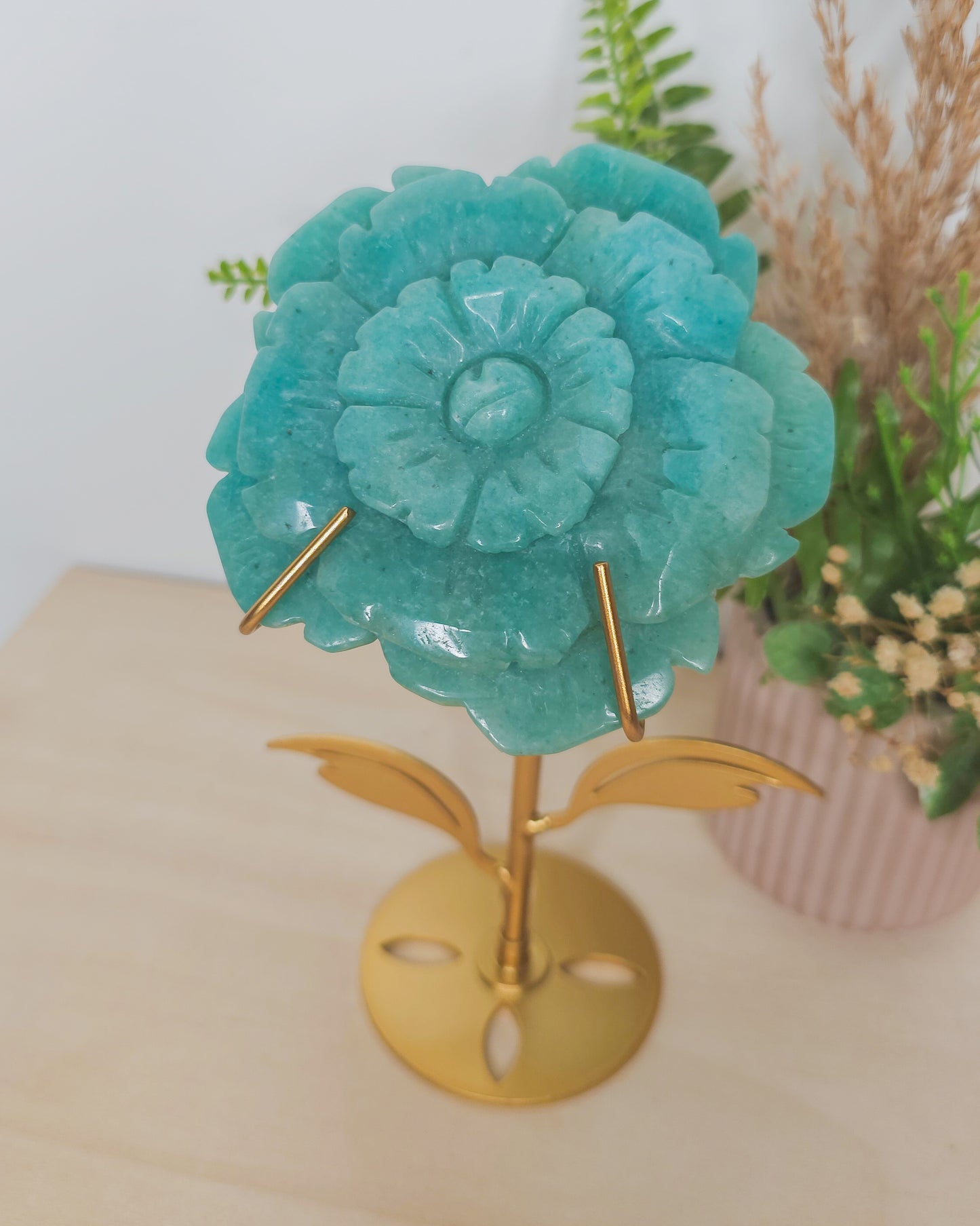 Amazonite crystal flower carving displayed on a black metal stand. The soothing blue-green stone is intricately shaped into a blooming flower, representing harmony, truth, and heart-centered healing.