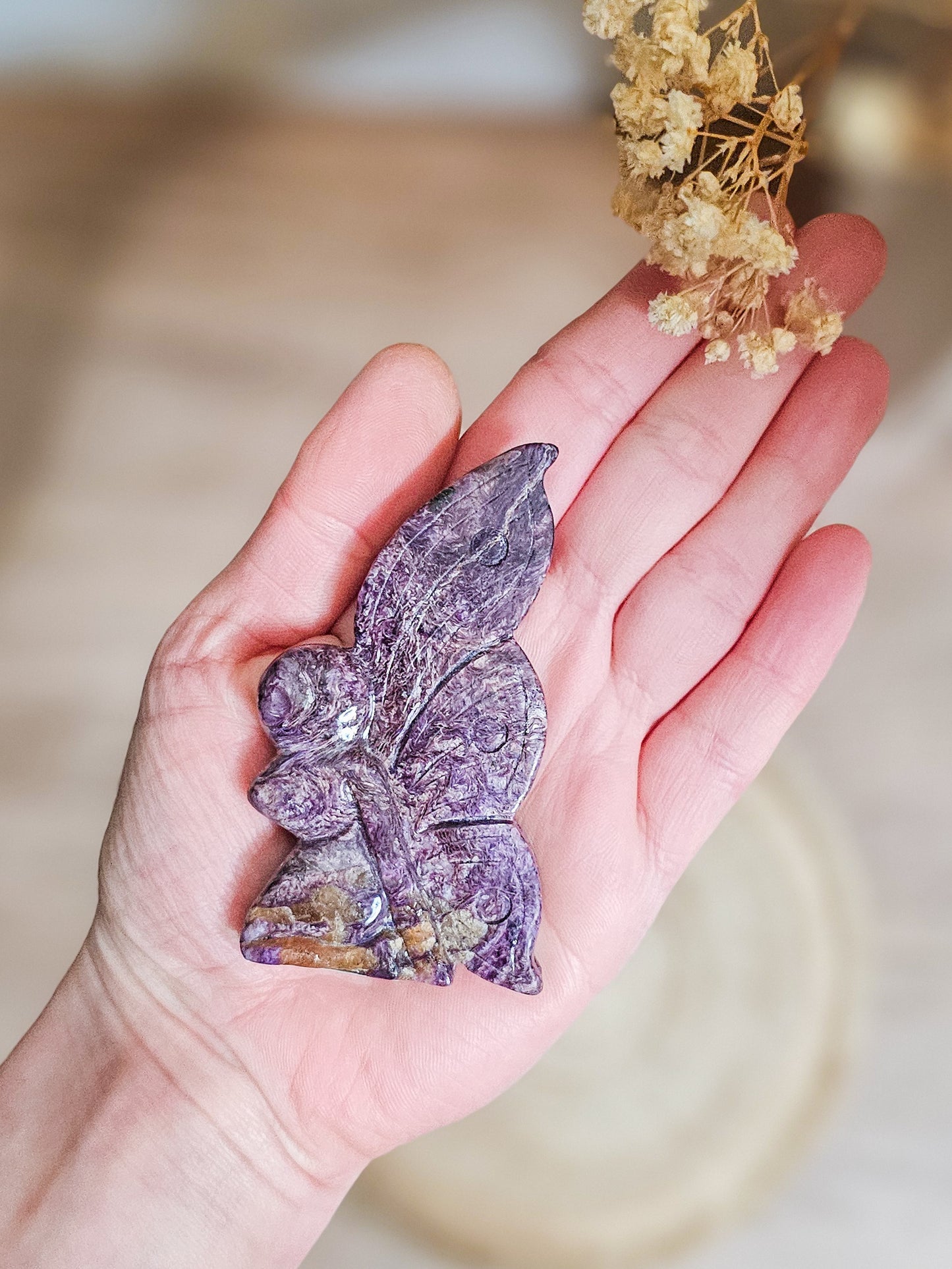 Close-up of carved Charoite fairy, highlighting swirling violet patterns and translucent crystal texture