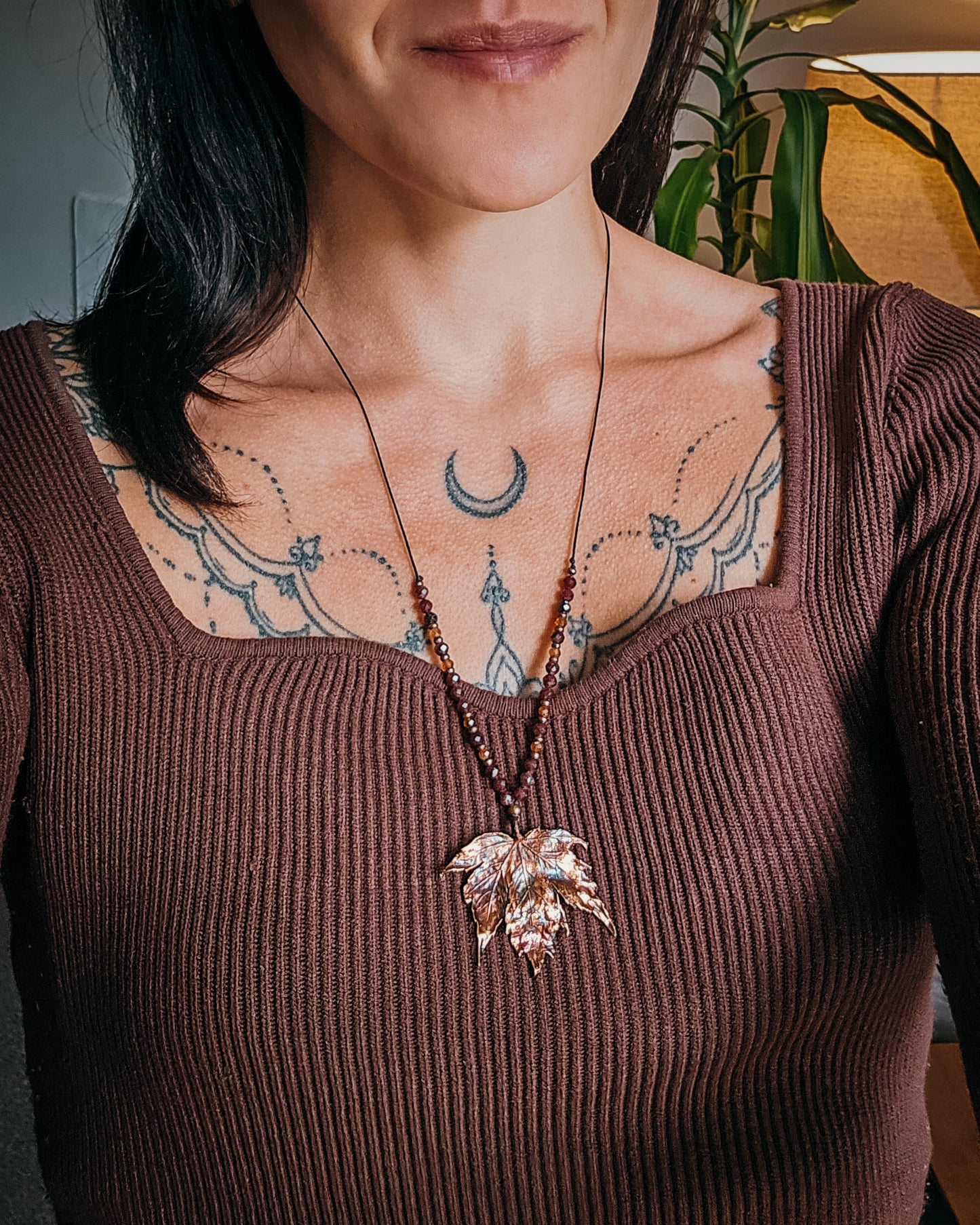 Handmade Copper electroformed Necklace with maple leaf pendant and Garnet crystal beads on a textured surface with leaves