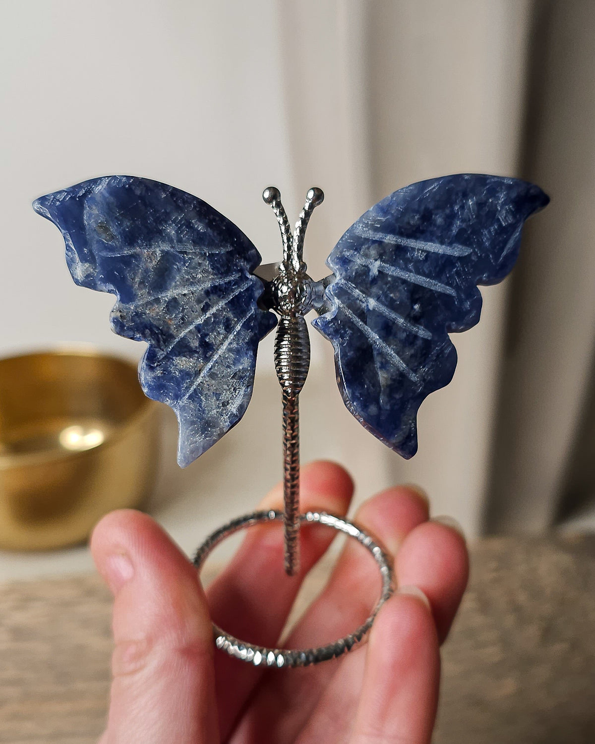 Sodalite butterfly carving on a silver-tone metal stand, featuring deep blue colouring with natural white veining.