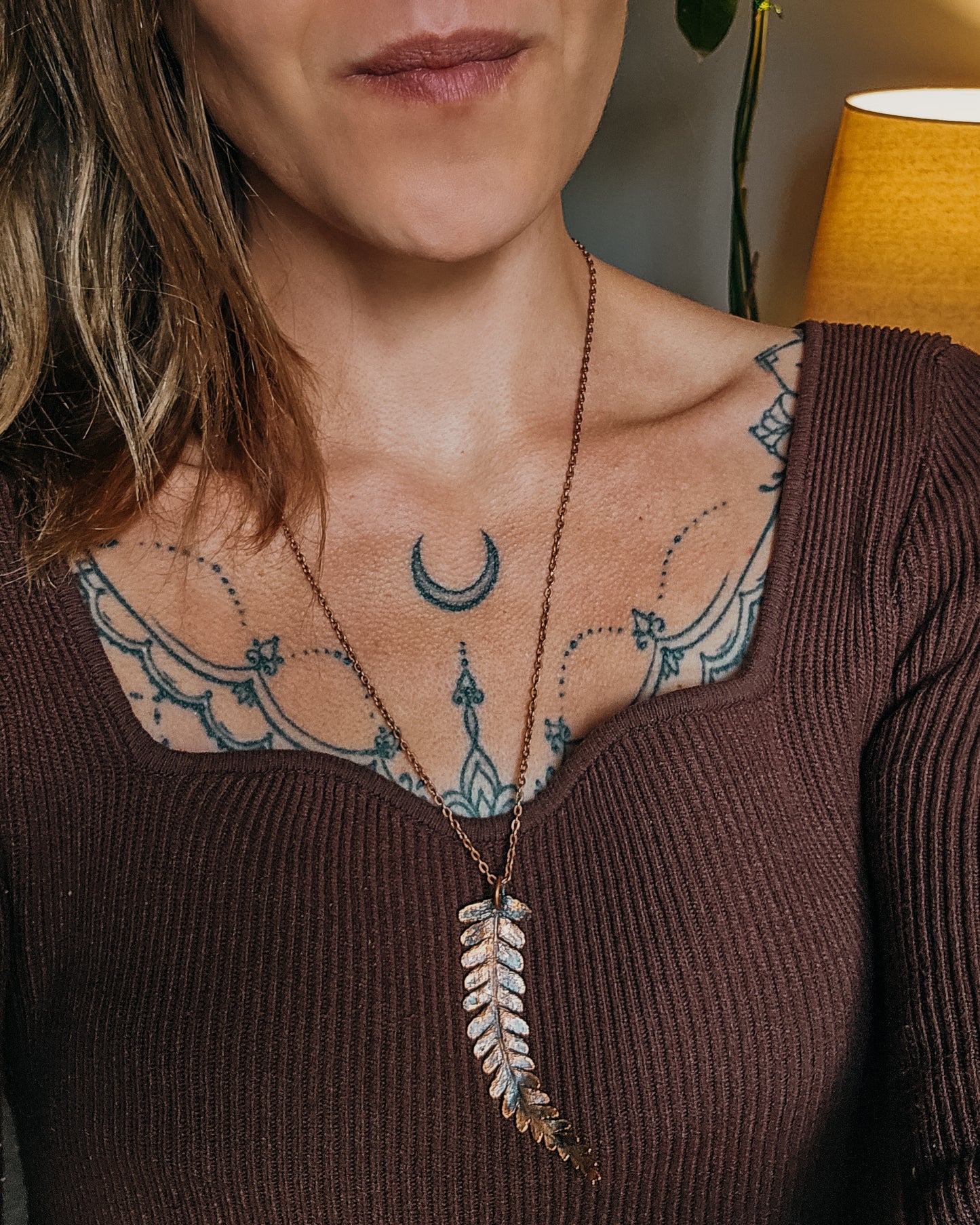 Woman with tattoos wearing One-of-a-kind copper electroformed fern amulet, handcrafted in Scotland. A unique botanical statement necklace for nature lovers.