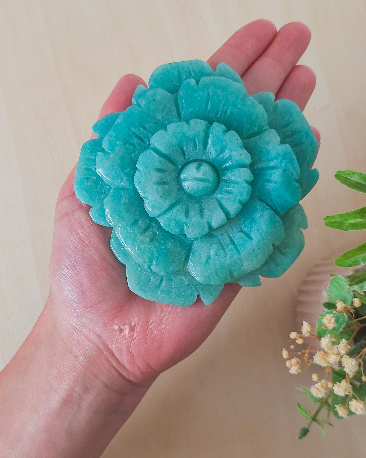 Amazonite crystal flower carving displayed on a black metal stand. The soothing blue-green stone is intricately shaped into a blooming flower, representing harmony, truth, and heart-centered healing.