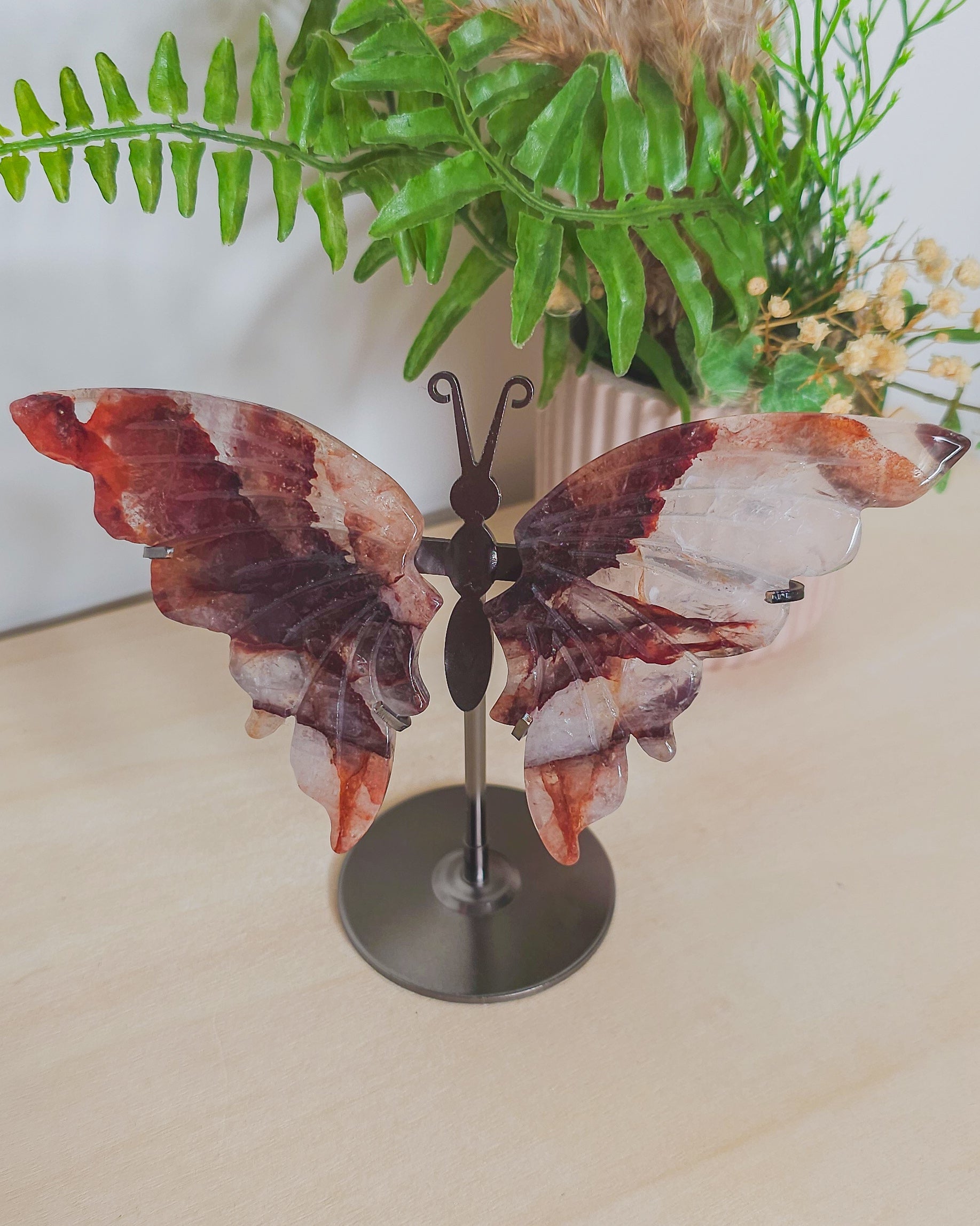 Fire Quartz butterfly wings on metal stand, featuring red Hematite inclusions in clear quartz, symbolizing transformation, strength, and focus.
