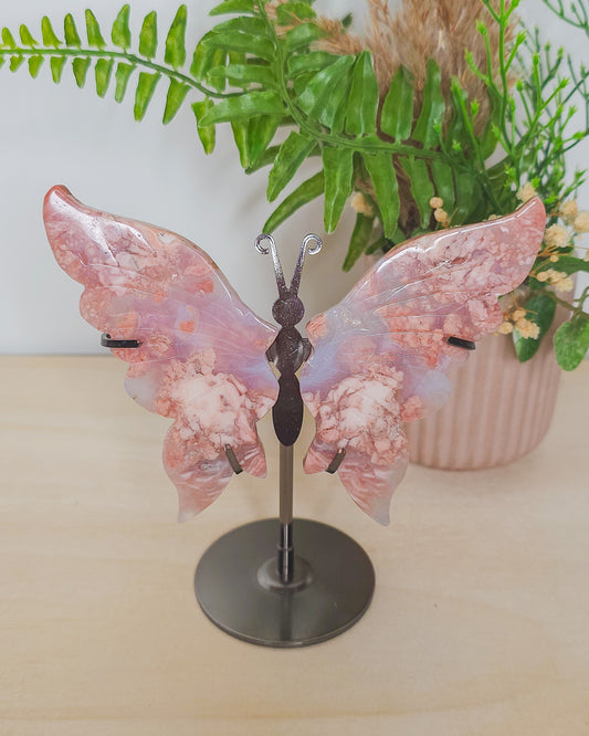 Delicate pink butterfly wings carved from Cotton Candy Agate, displayed upright on a stand. The crystal features soft pastel hues and banded patterns, evoking a gentle, heart-centered energy.