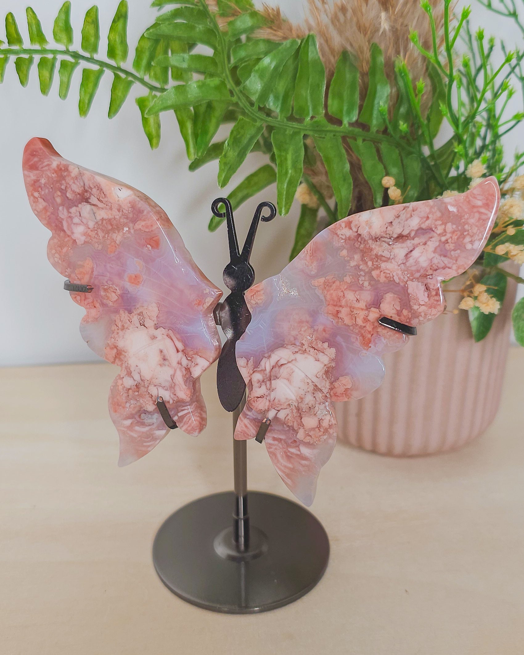 Delicate pink butterfly wings carved from Cotton Candy Agate, displayed upright on a stand. The crystal features soft pastel hues and banded patterns, evoking a gentle, heart-centered energy.