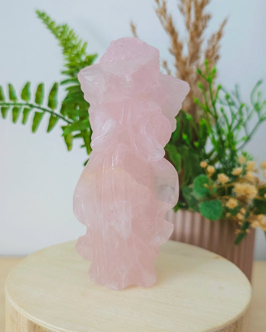 Rose Quartz angel figurine Carving standing upright, polished to a smooth finish with soft pink tones. The carving features outstretched wings and gentle contours, symbolizing love, compassion, and emotional healing. Displayed against a neutral background.