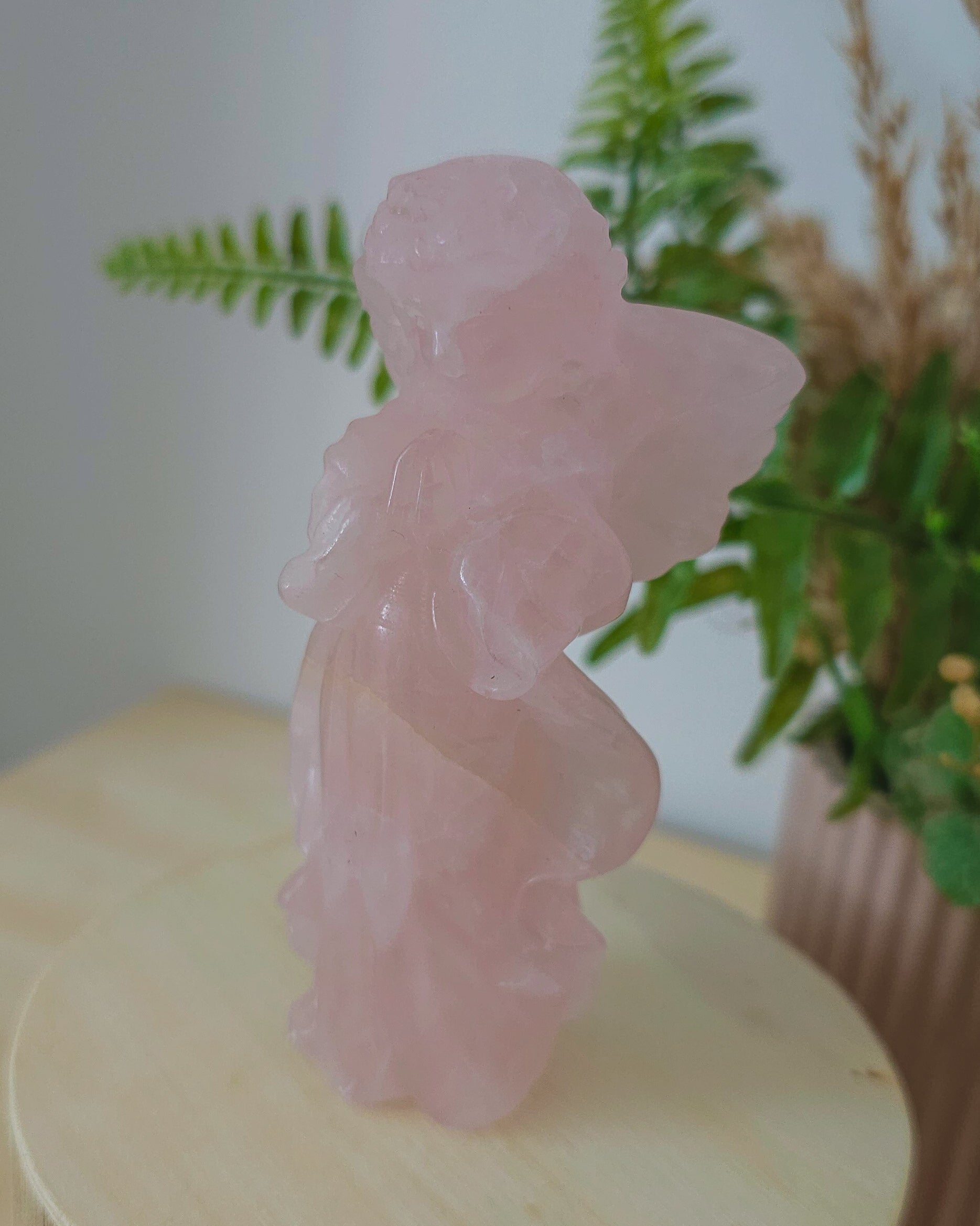 Rose Quartz angel figurine Carving standing upright, polished to a smooth finish with soft pink tones. The carving features outstretched wings and gentle contours, symbolizing love, compassion, and emotional healing. Displayed against a neutral background.