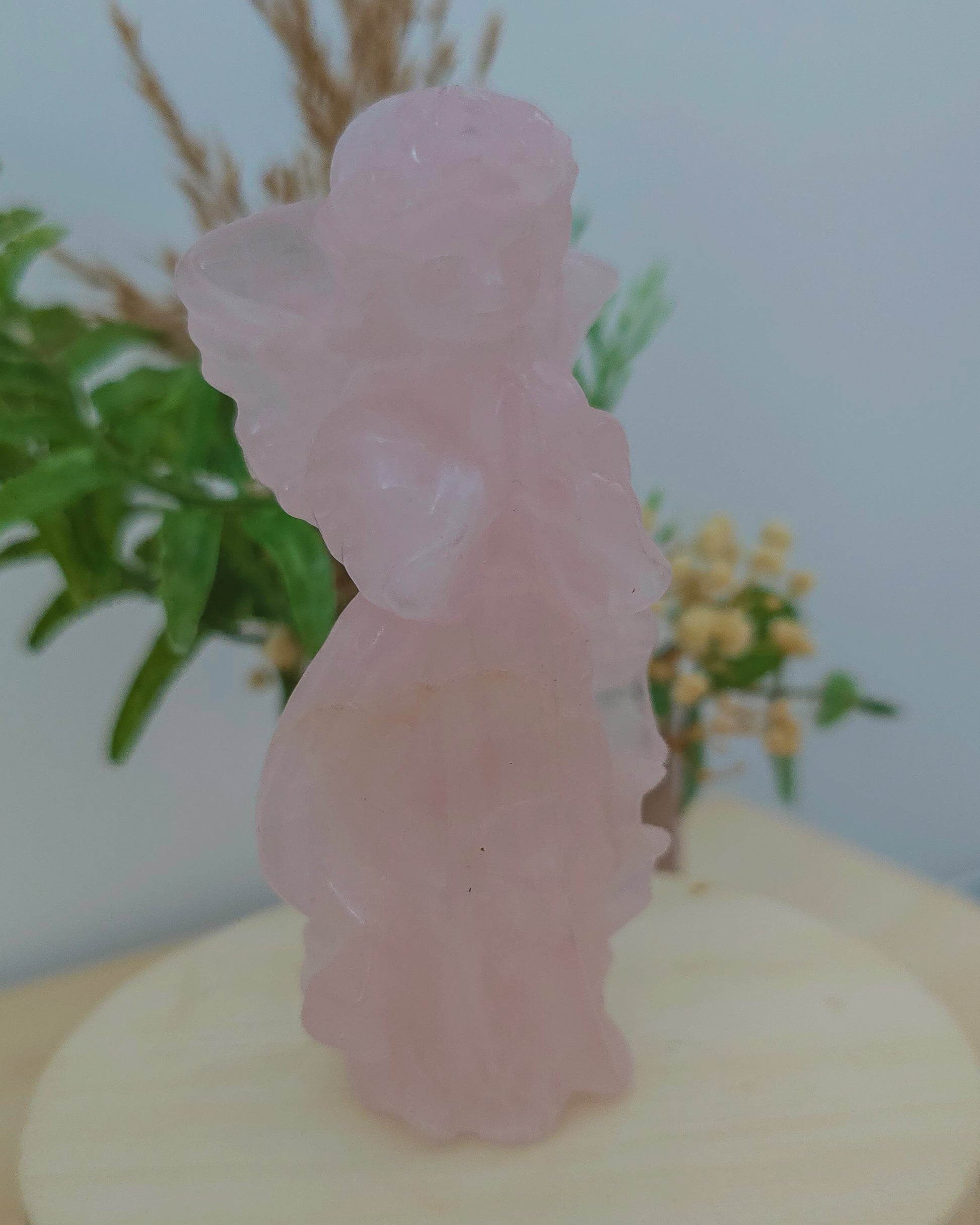 Rose Quartz angel figurine Carving standing upright, polished to a smooth finish with soft pink tones. The carving features outstretched wings and gentle contours, symbolizing love, compassion, and emotional healing. Displayed against a neutral background.