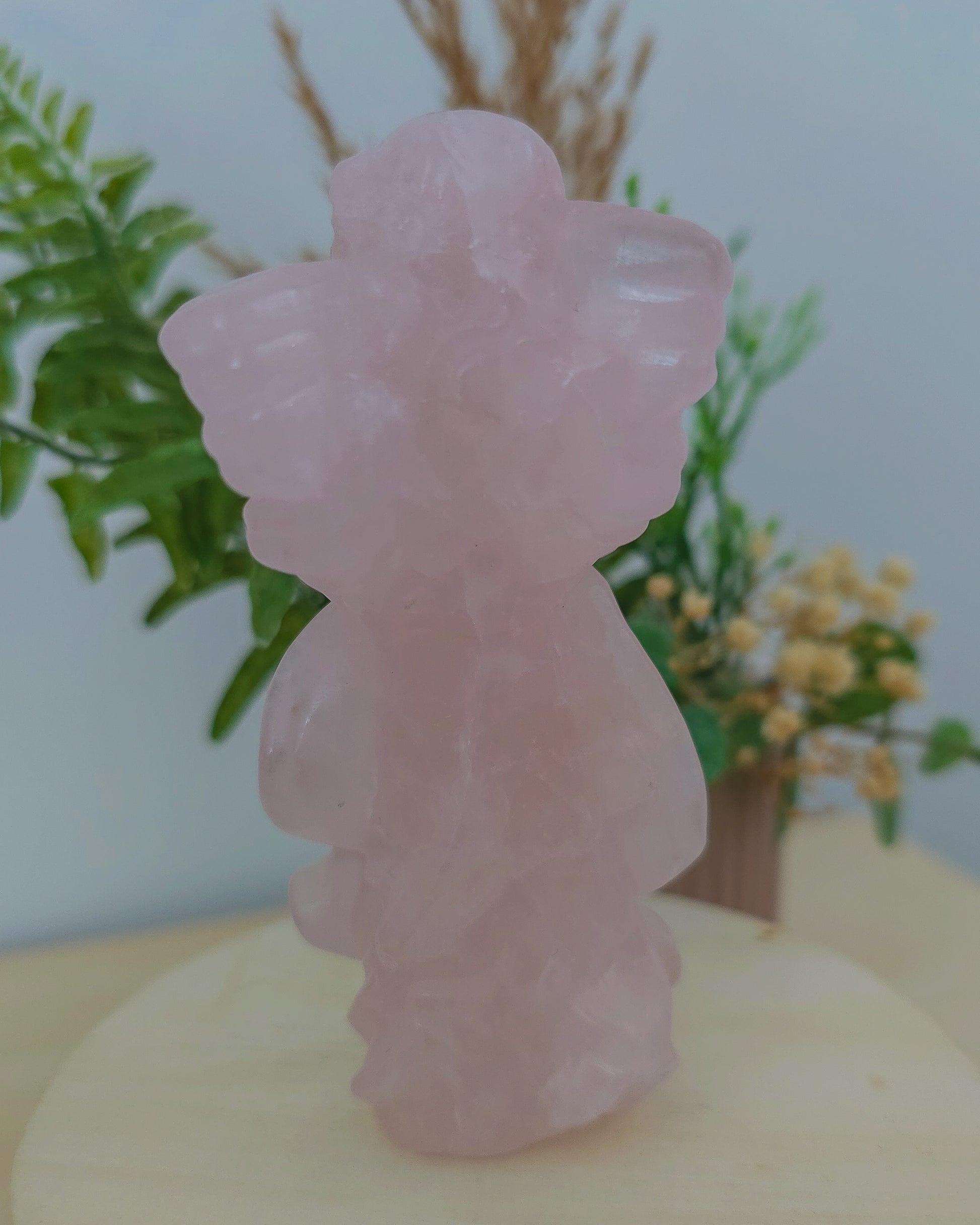 Rose Quartz angel figurine Carving standing upright, polished to a smooth finish with soft pink tones. The carving features outstretched wings and gentle contours, symbolizing love, compassion, and emotional healing. Displayed against a neutral background.
