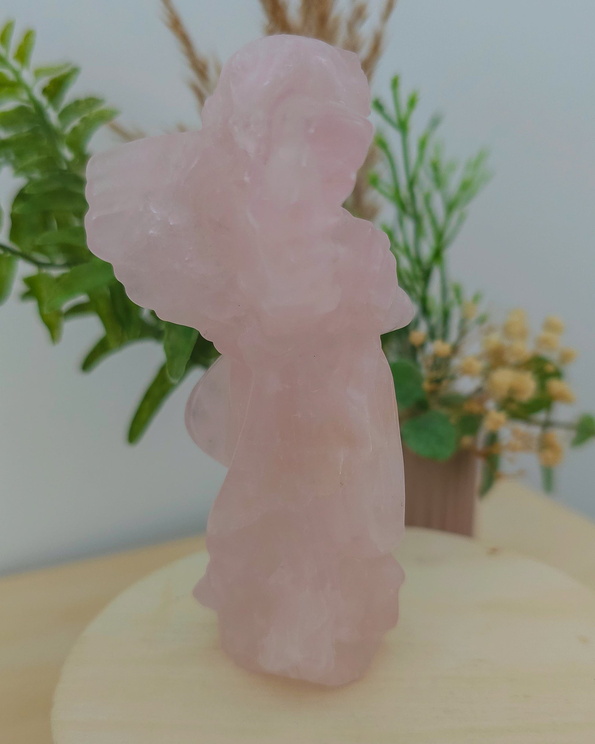 Rose Quartz angel figurine Carving standing upright, polished to a smooth finish with soft pink tones. The carving features outstretched wings and gentle contours, symbolizing love, compassion, and emotional healing. Displayed against a neutral background.