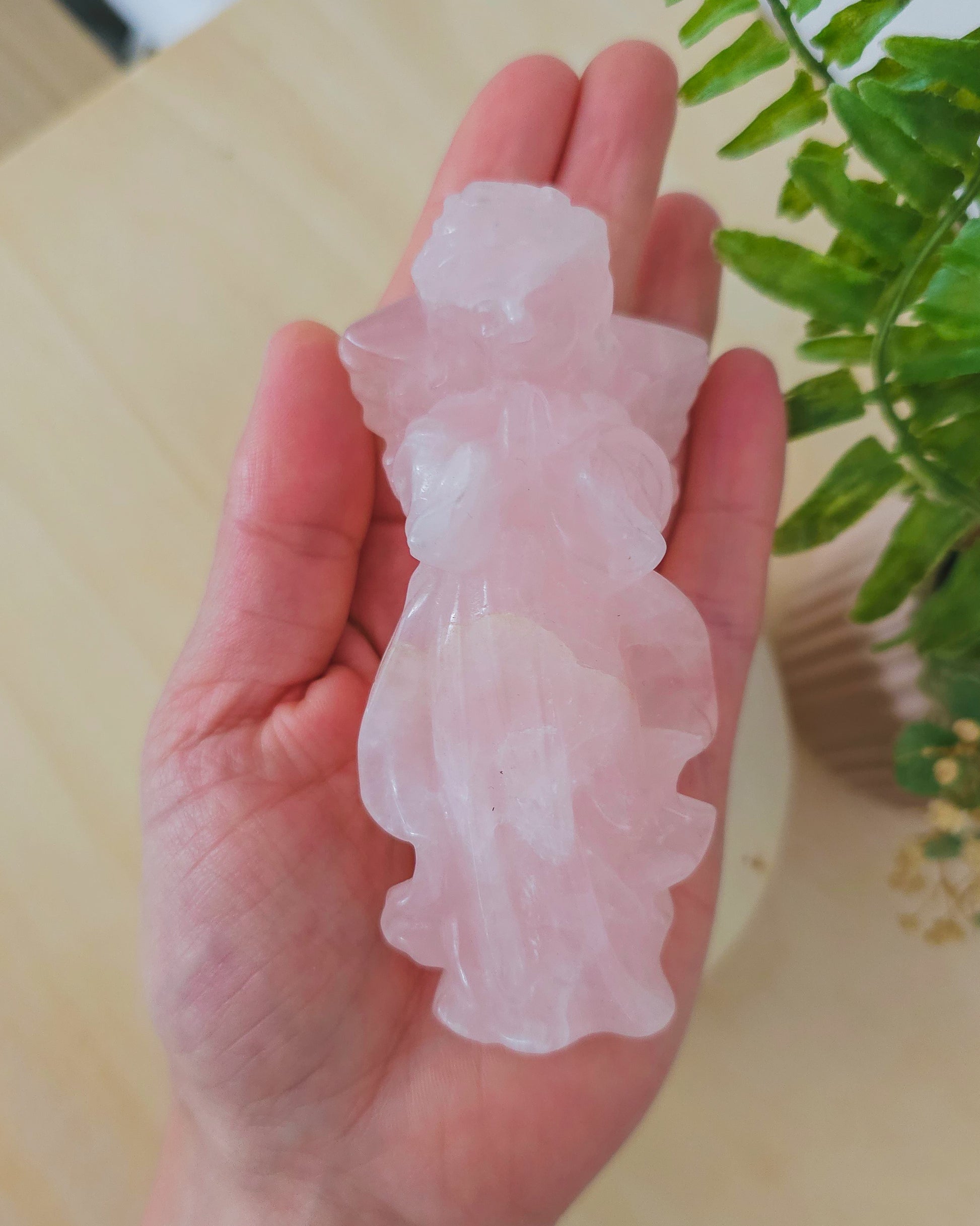 Rose Quartz angel figurine Carving standing upright, polished to a smooth finish with soft pink tones. The carving features outstretched wings and gentle contours, symbolizing love, compassion, and emotional healing. Displayed against a neutral background.
