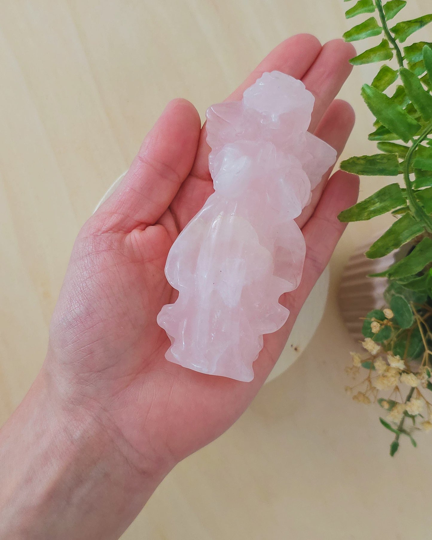 Rose Quartz angel figurine Carving standing upright, polished to a smooth finish with soft pink tones. The carving features outstretched wings and gentle contours, symbolizing love, compassion, and emotional healing. Displayed against a neutral background.