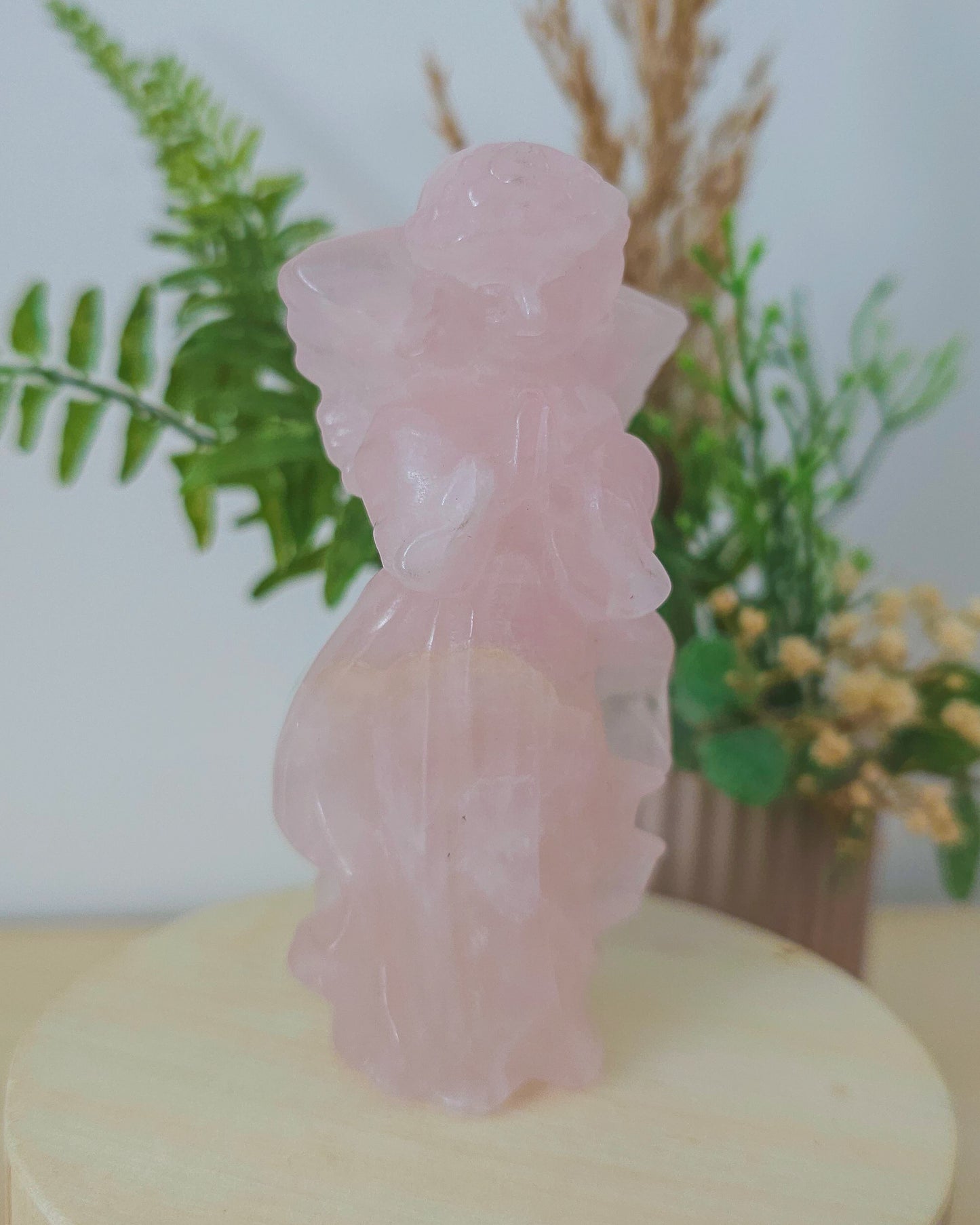 Rose Quartz angel figurine Carving standing upright, polished to a smooth finish with soft pink tones. The carving features outstretched wings and gentle contours, symbolizing love, compassion, and emotional healing. Displayed against a neutral background.