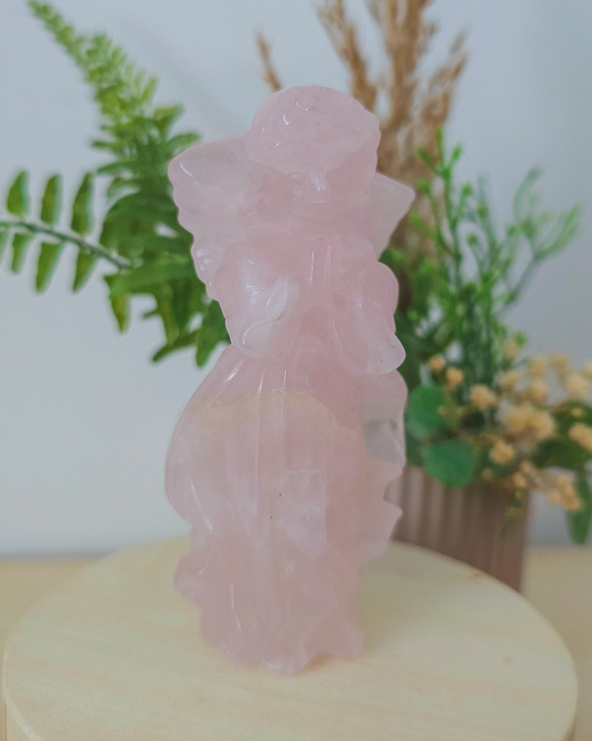 Rose Quartz angel figurine Carving standing upright, polished to a smooth finish with soft pink tones. The carving features outstretched wings and gentle contours, symbolizing love, compassion, and emotional healing. Displayed against a neutral background.