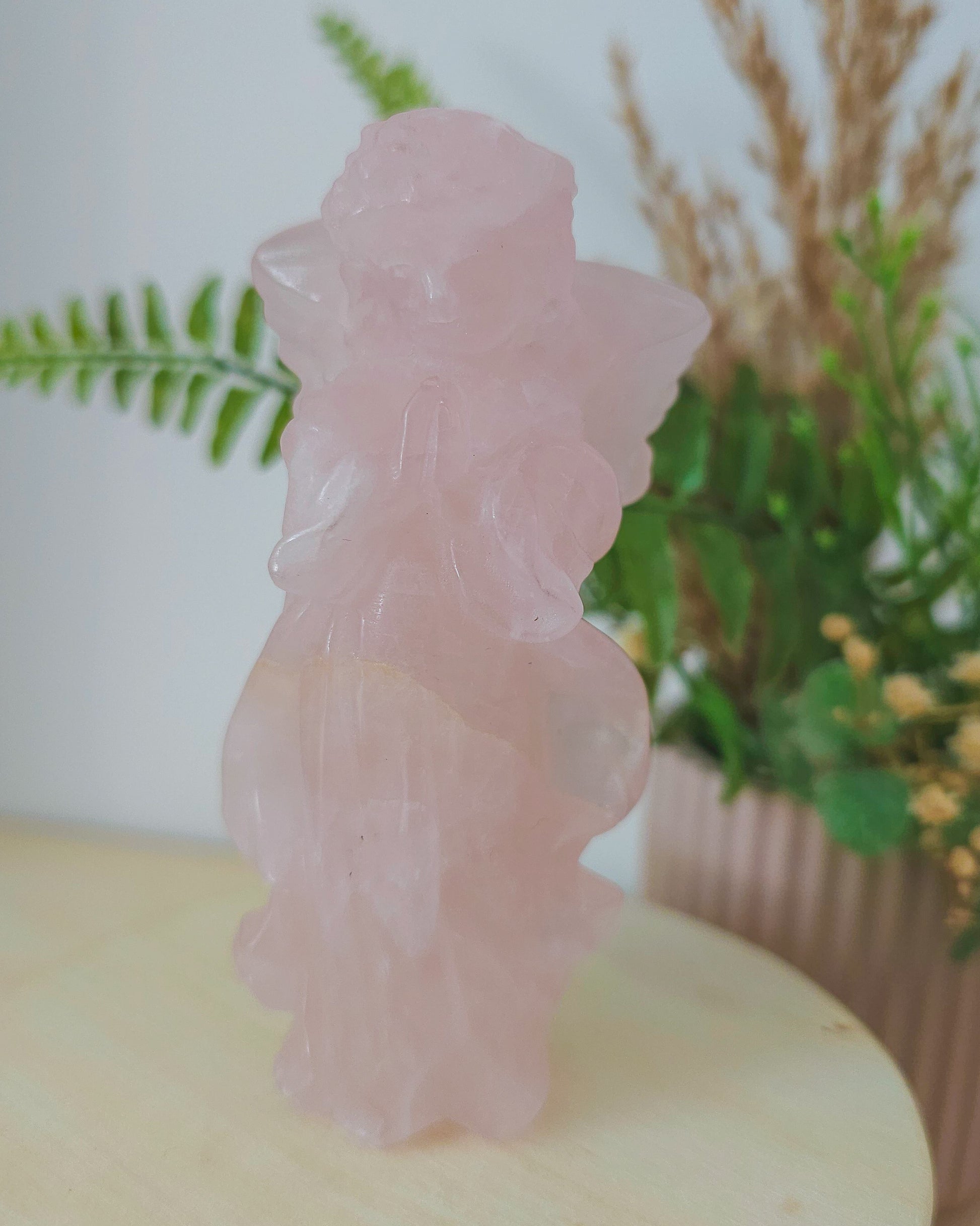 Rose Quartz angel figurine Carving standing upright, polished to a smooth finish with soft pink tones. The carving features outstretched wings and gentle contours, symbolizing love, compassion, and emotional healing. Displayed against a neutral background.