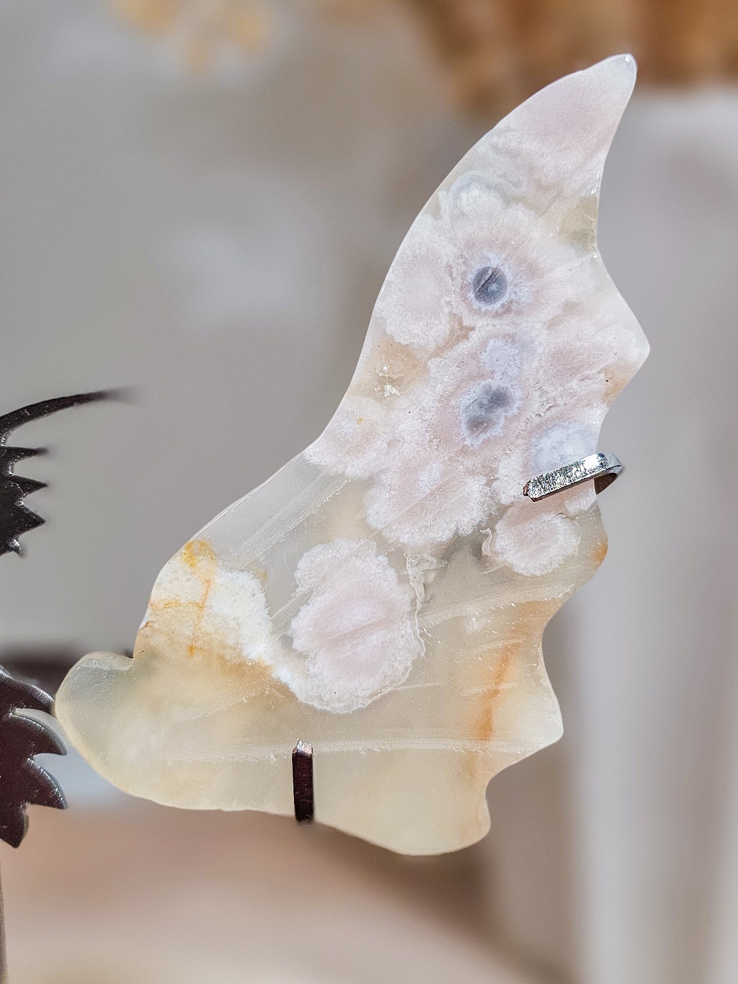Pair of carved fluorescent Flower Agate dragon wings on acrylic stand, showing soft pink floral patterns and translucent crystal texture