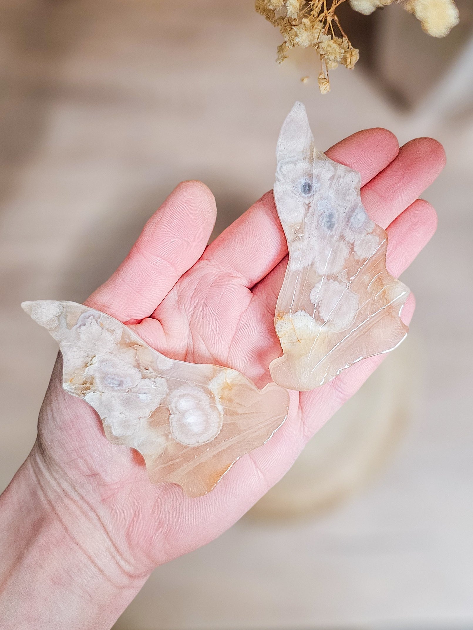 Pair of carved fluorescent Flower Agate dragon wings on acrylic stand, showing soft pink floral patterns and translucent crystal texture