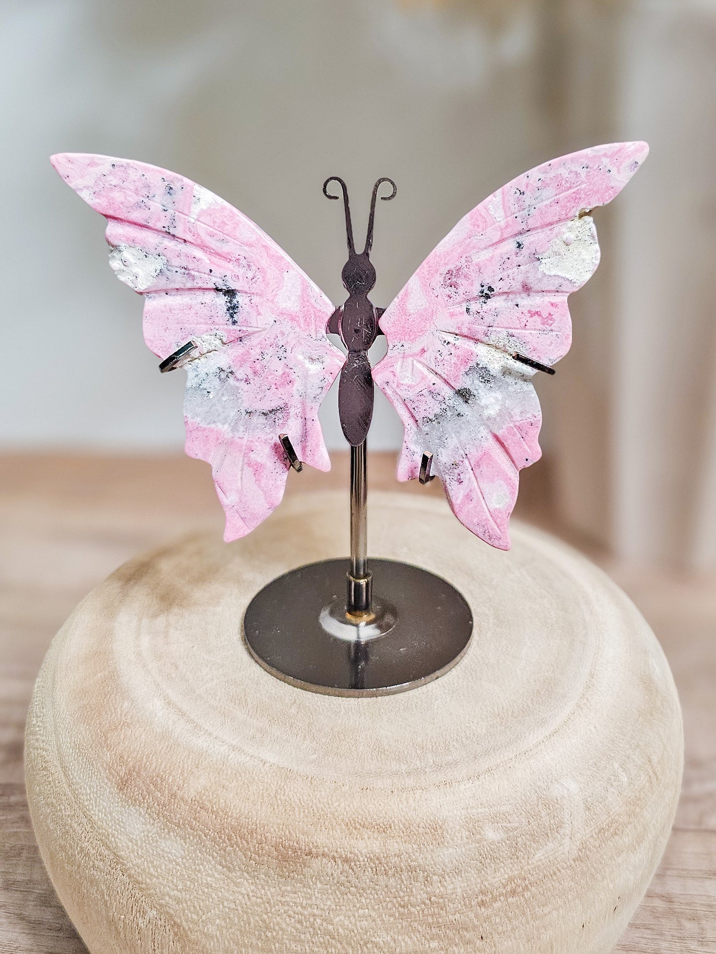 Carved Peruvian Rhodonite butterfly wings on display stand, showing soft pink tones and natural stone patterns