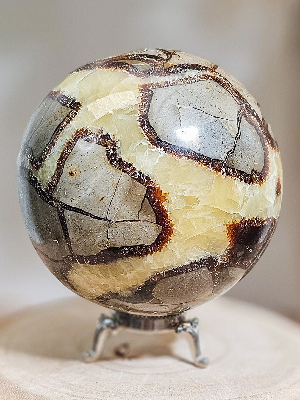 Fluorescent Septarian sphere on stand, polished brown and yellow stone with natural crackled patterns and glowing Calcite veins