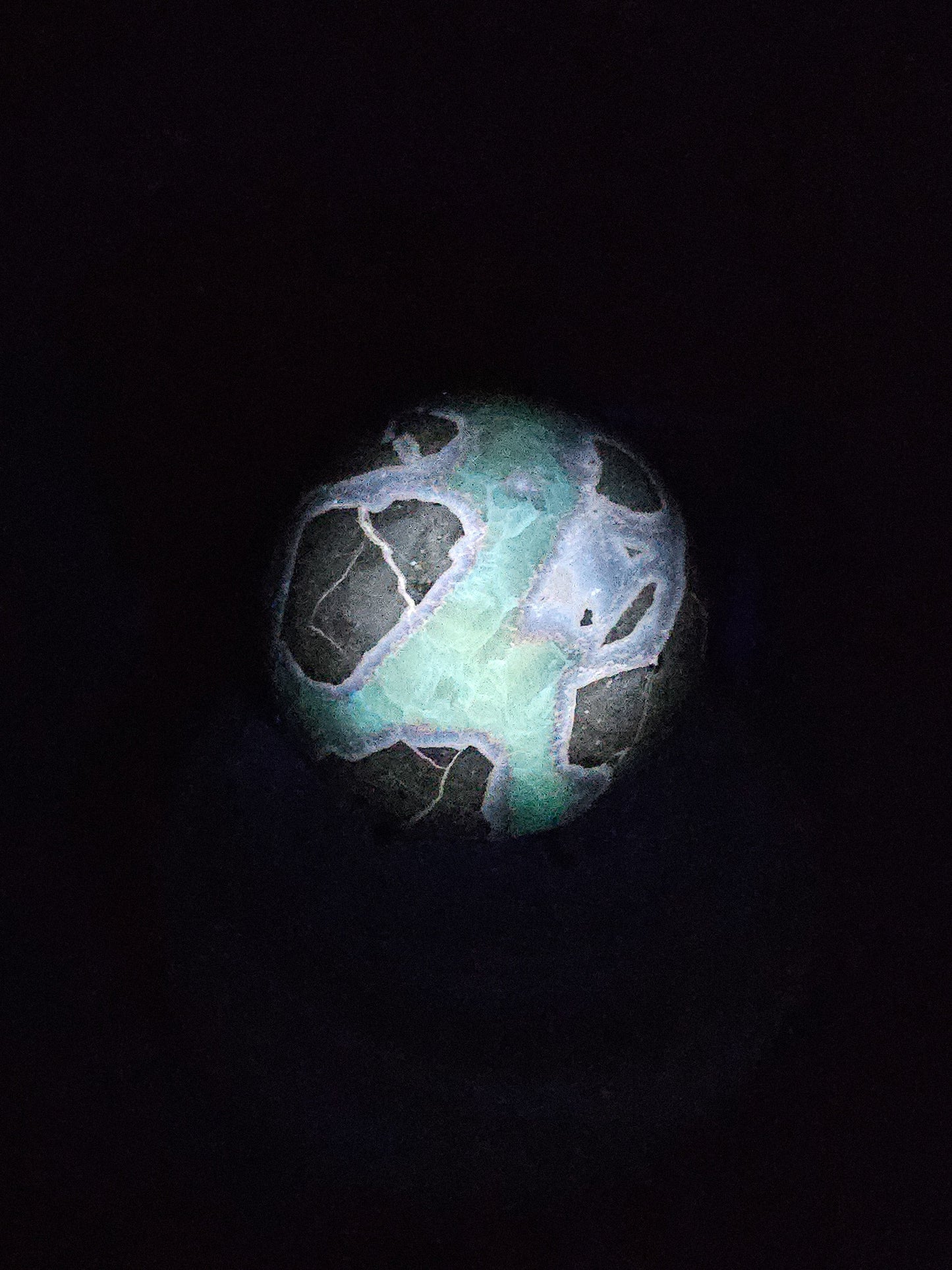 Polished Septarian sphere on stand, glowing under UV light to reveal fluorescent Calcite