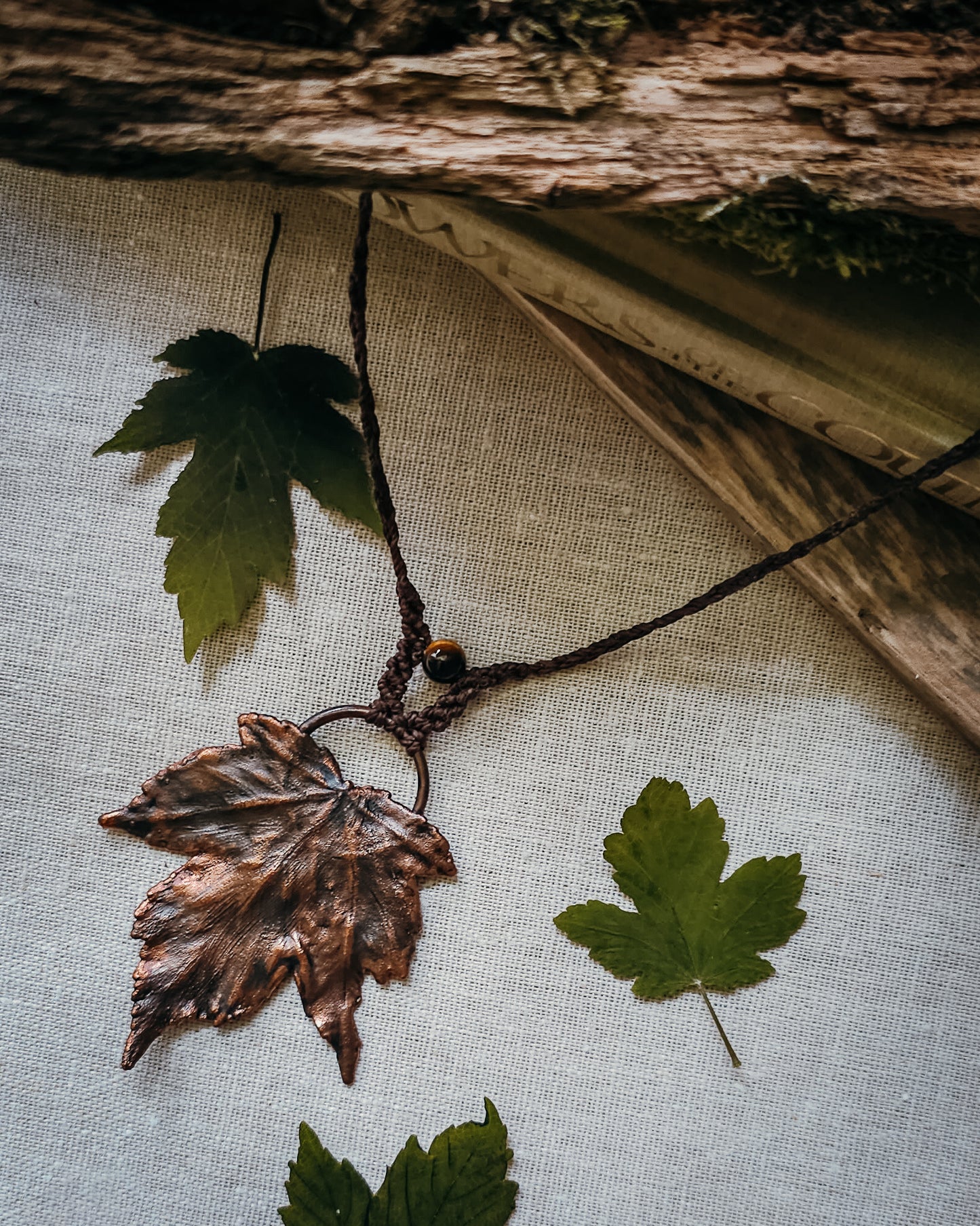 Handmade Copper electroformed Necklace with maple leaf pendant and Tiger's Eye bead on a textured surface with leaves