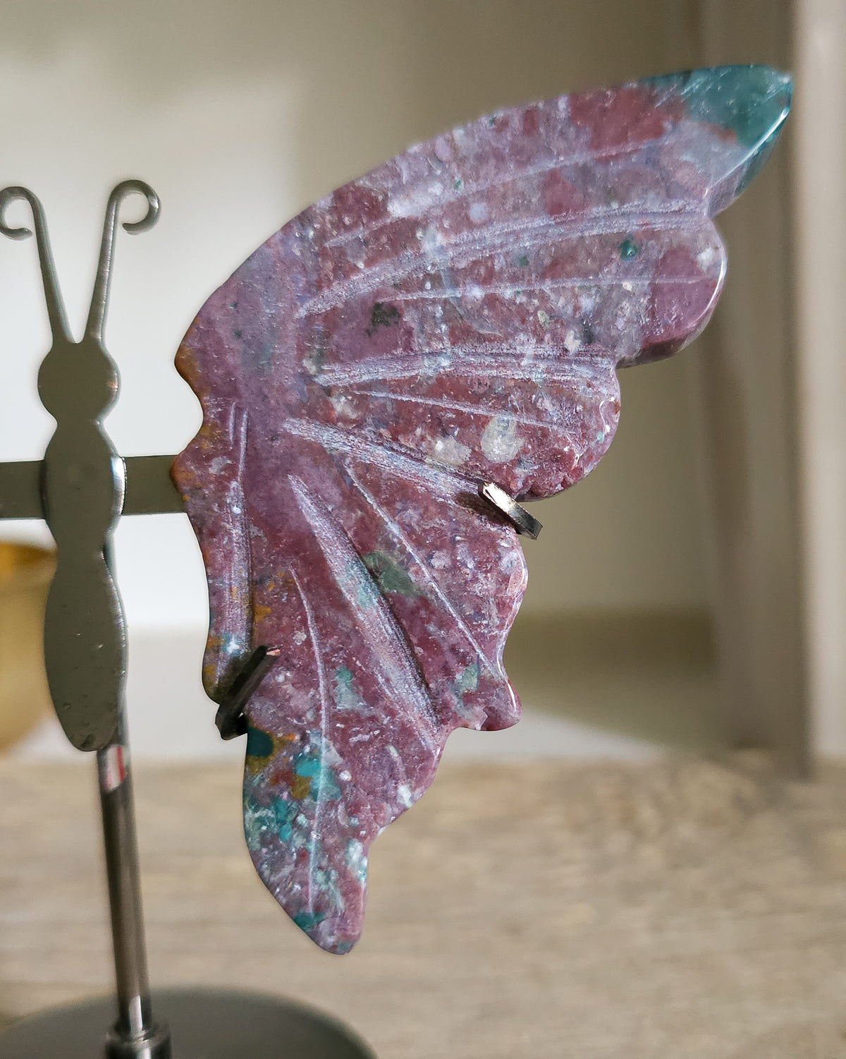 Jasper butterfly wings on a black metal stand, showing natural mauve, pink, green, turquoise and white patterns.. 