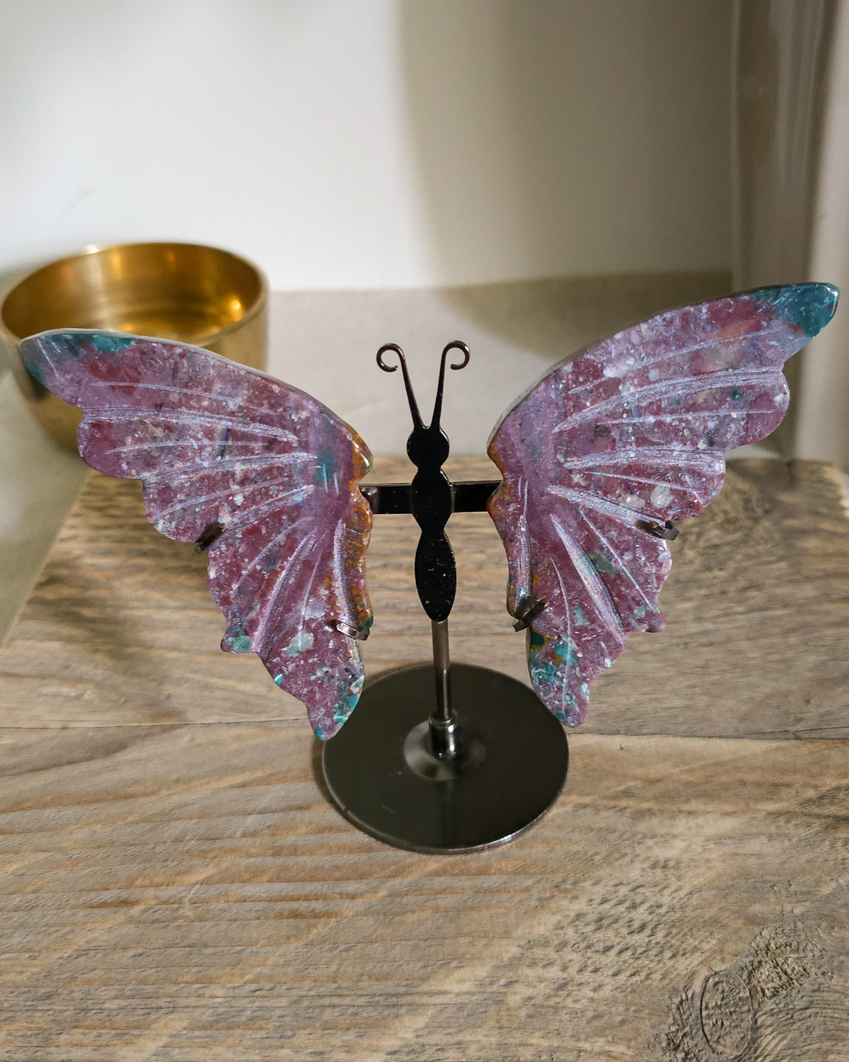 Jasper butterfly wings on a black metal stand, showing natural mauve, pink, green, turquoise and white patterns.. 