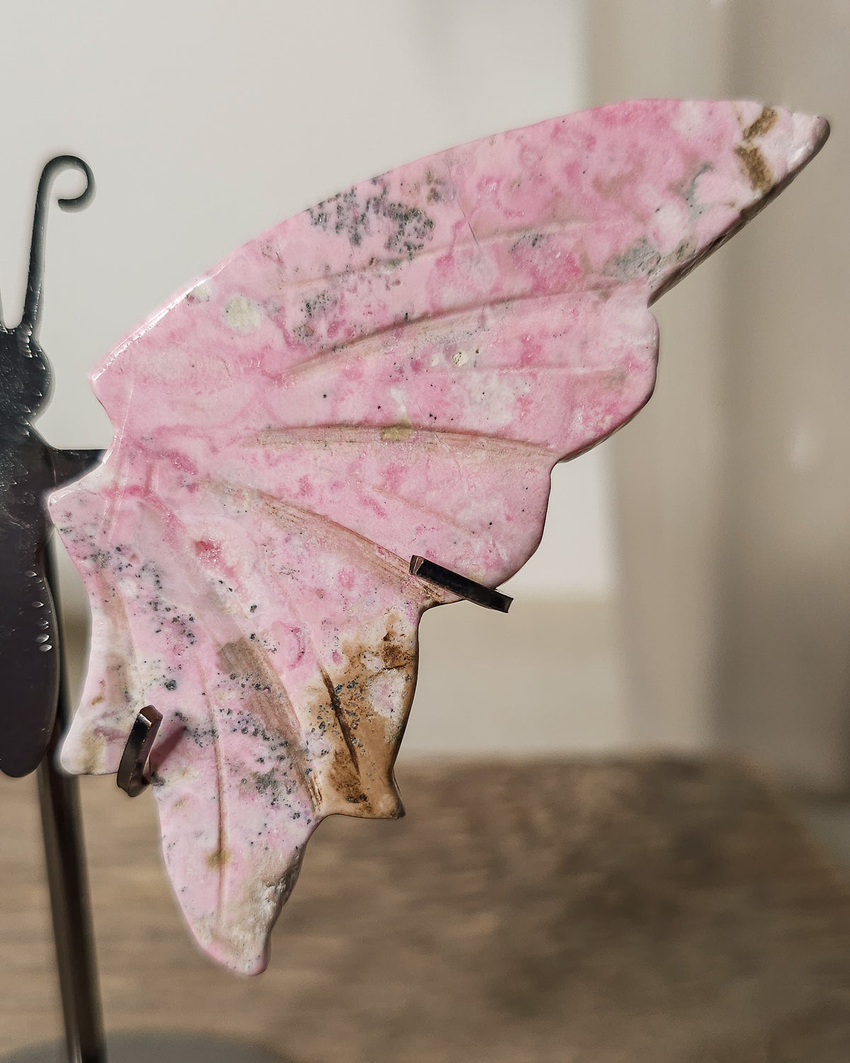 Peruvian Rhodonite crystal butterfly wings on a metal stand, with unique pink and dark markings. A meaningful gift or addition to your crystal collection.