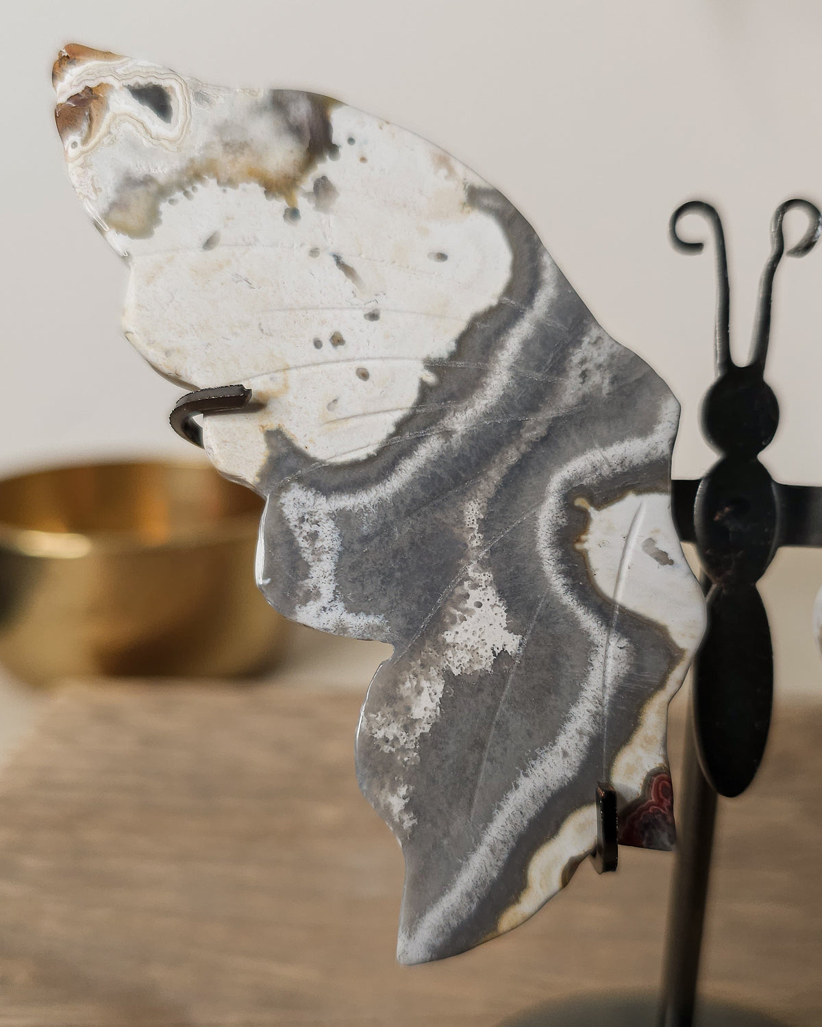 Grey and white Agate butterfly wings displayed on a metal stand, featuring soft natural banding and cloudy patterns.