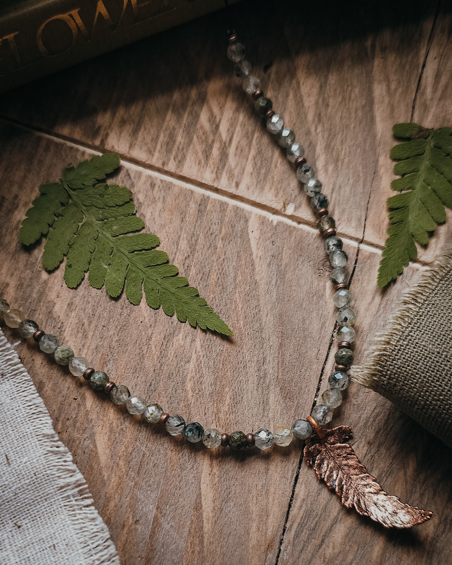 Necklace with copper electroformed fern leaf pendant and crystal Prehnite and Epidote beads on a wooden surface with fern leaves