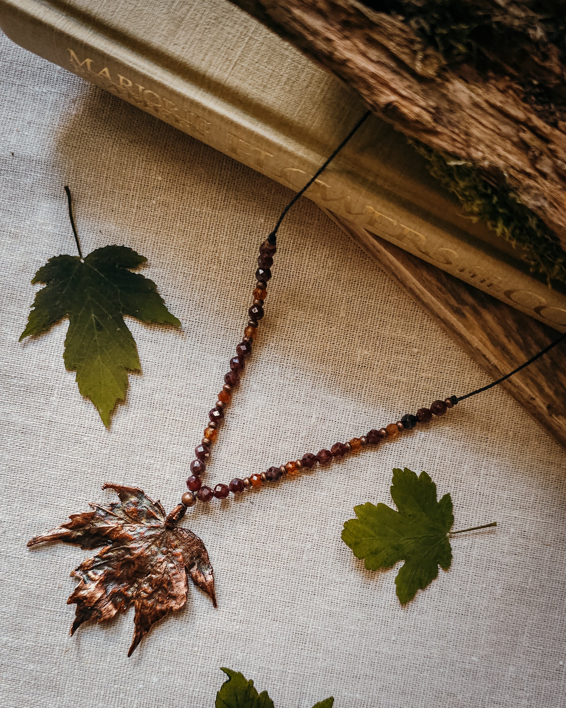 Copper electroformed Necklace with maple leaf pendant and crystal beads on a textured surface with leaves