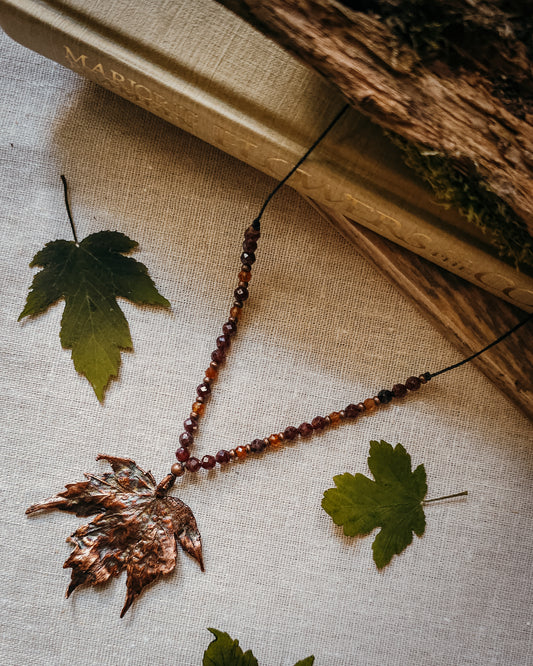 Copper electroformed Necklace with maple leaf pendant and crystal beads on a textured surface with leaves