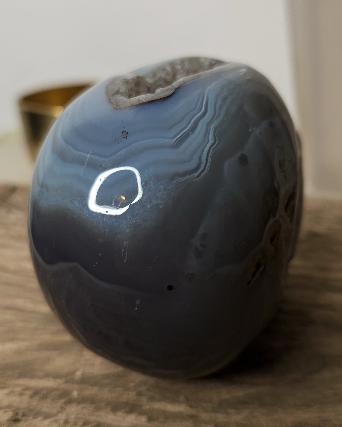 Blue Agate skull carving with layered pale blue and grey bands, a natural brown inclusion along the side and a sparkling druzy crystal cavity at the top.