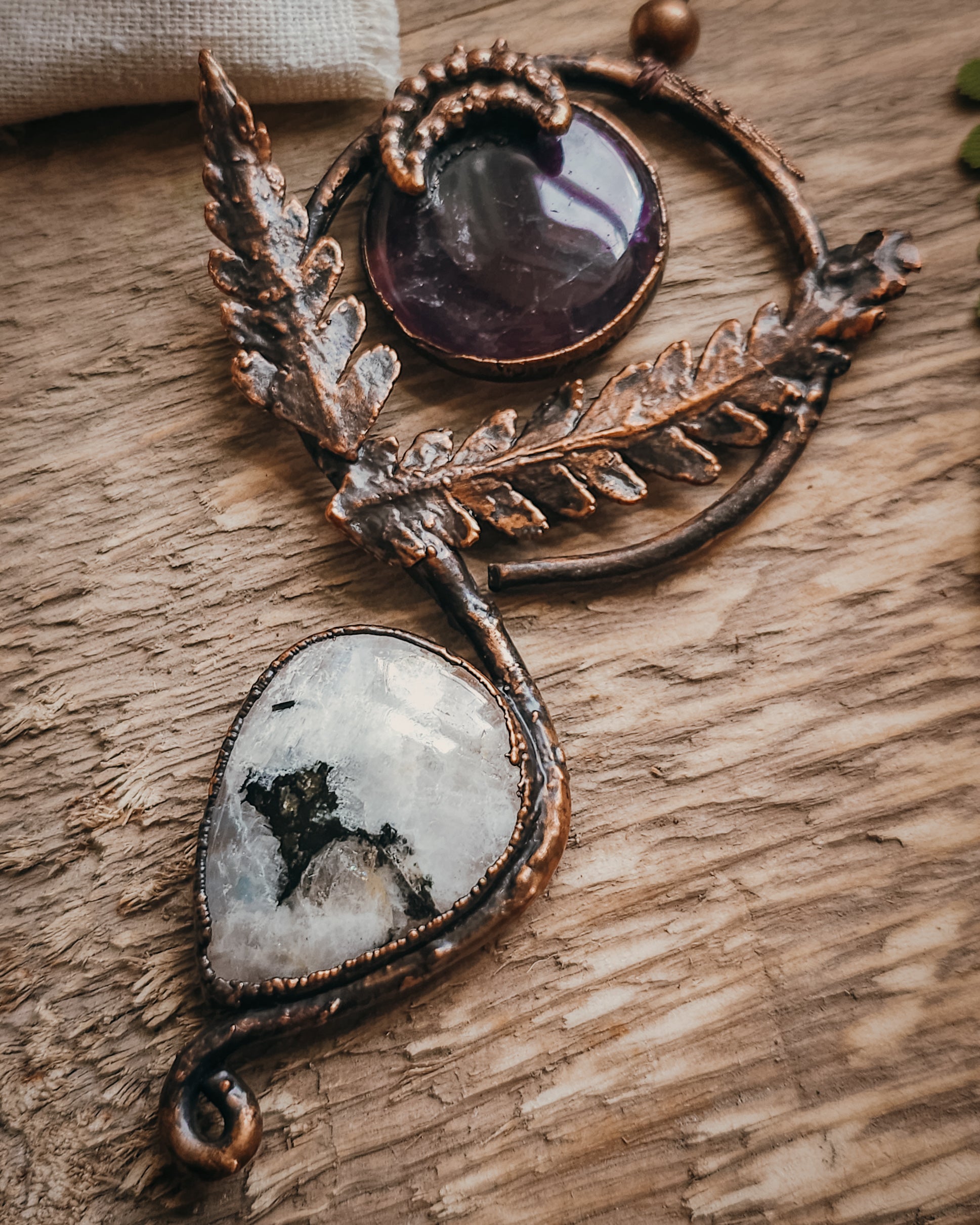 Copper electroformed Ornate pendant with amehtyst, Moonstone and fern leaves on a wooden surface with leaves
