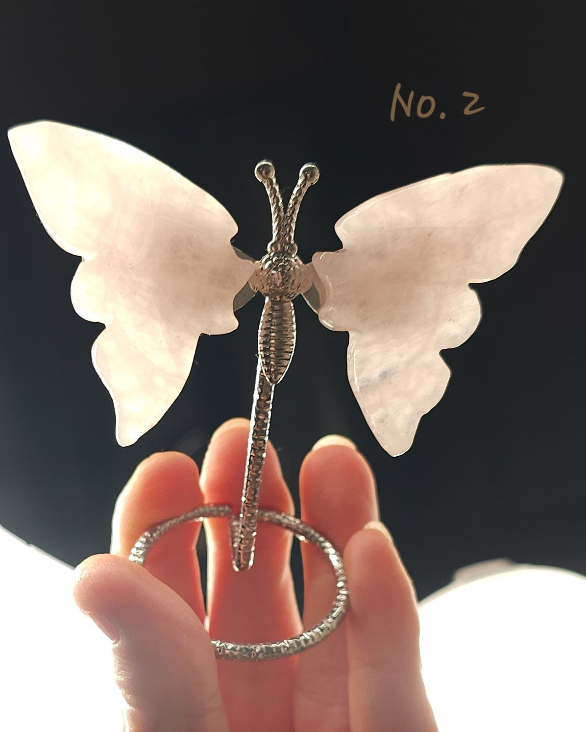 Polished rose quartz crystal butterfly carving with soft pink wings on a silver-tone display stand. 
