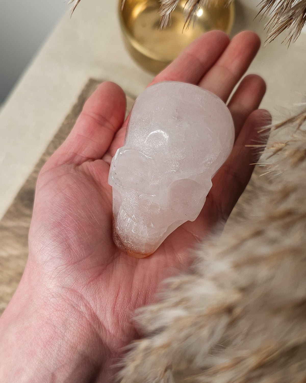 Rose Quartz crystal skull with natural red Hematite inclusions, showing soft pink tones and a reddish patch at the base.