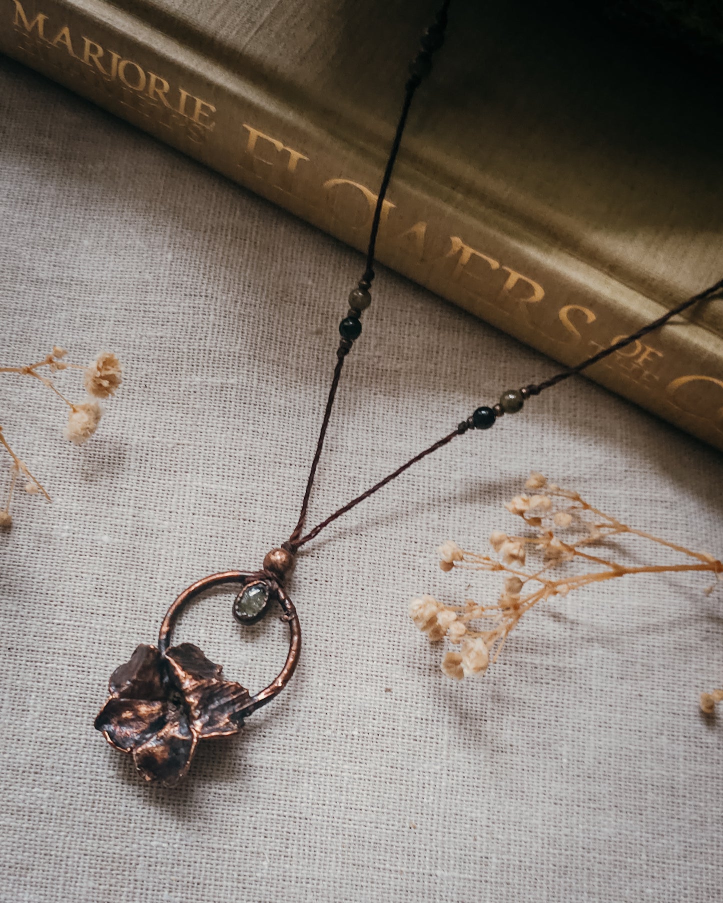 Handcrafted copper electroformed Primrose flower necklace featuring a natural Green Tourmaline stone, green and pink Tourmaline beads, brass accent beads on an adjustable cord. Created from a real Primrose flower gathered in Scotland and inspired by woodland folklore, renewal, and the magic of hidden pathways.