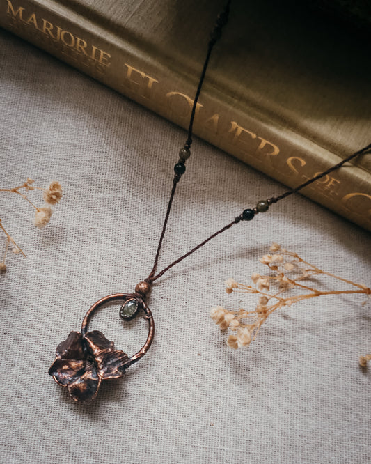 Handcrafted copper electroformed Primrose flower necklace featuring a natural Green Tourmaline stone, green and pink Tourmaline beads, brass accent beads on an adjustable cord. Created from a real Primrose flower gathered in Scotland and inspired by woodland folklore, renewal, and the magic of hidden pathways.