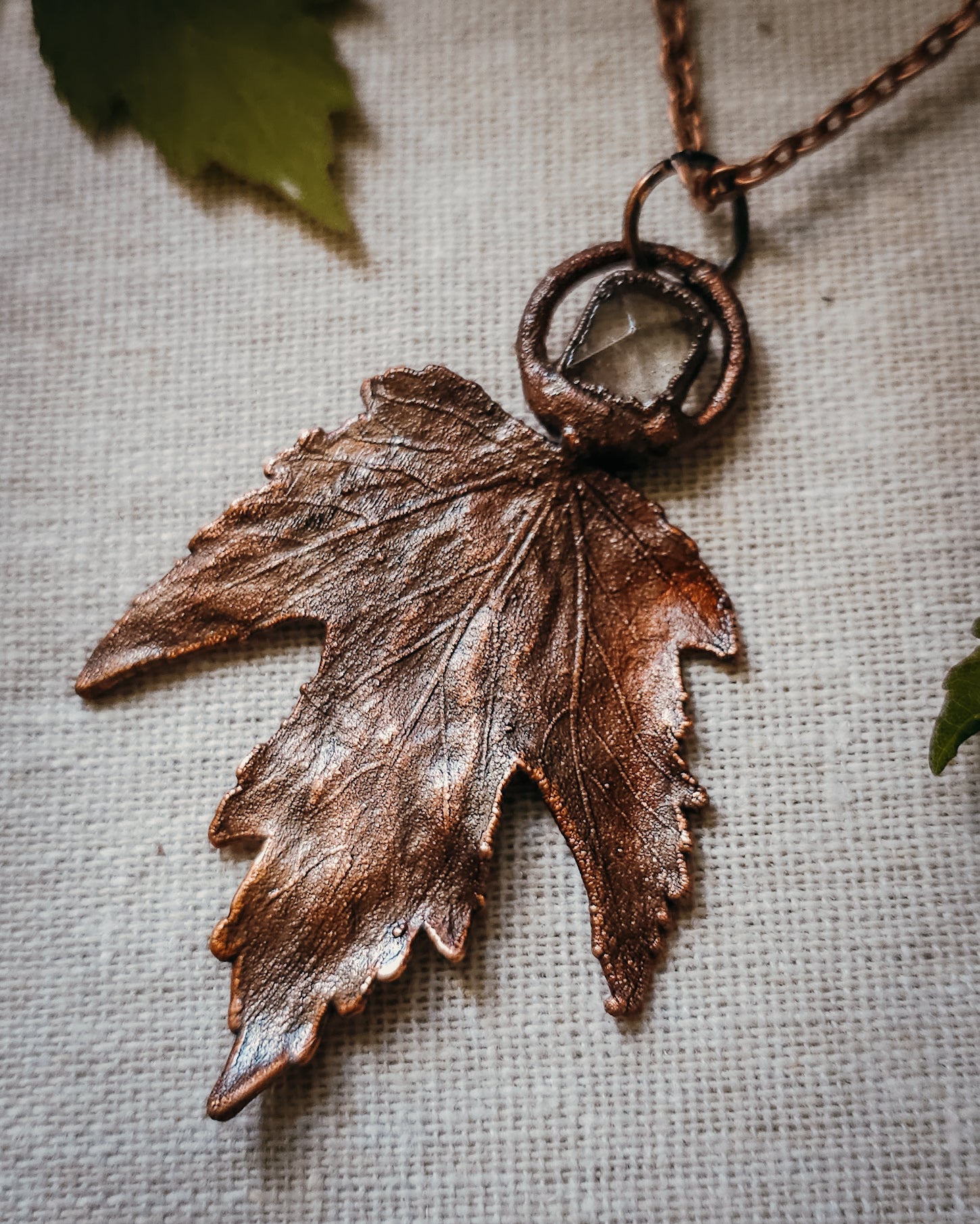 Copper electroformed Necklace with maple leaf pendant and Quartz crystal on a textured surface with leaves