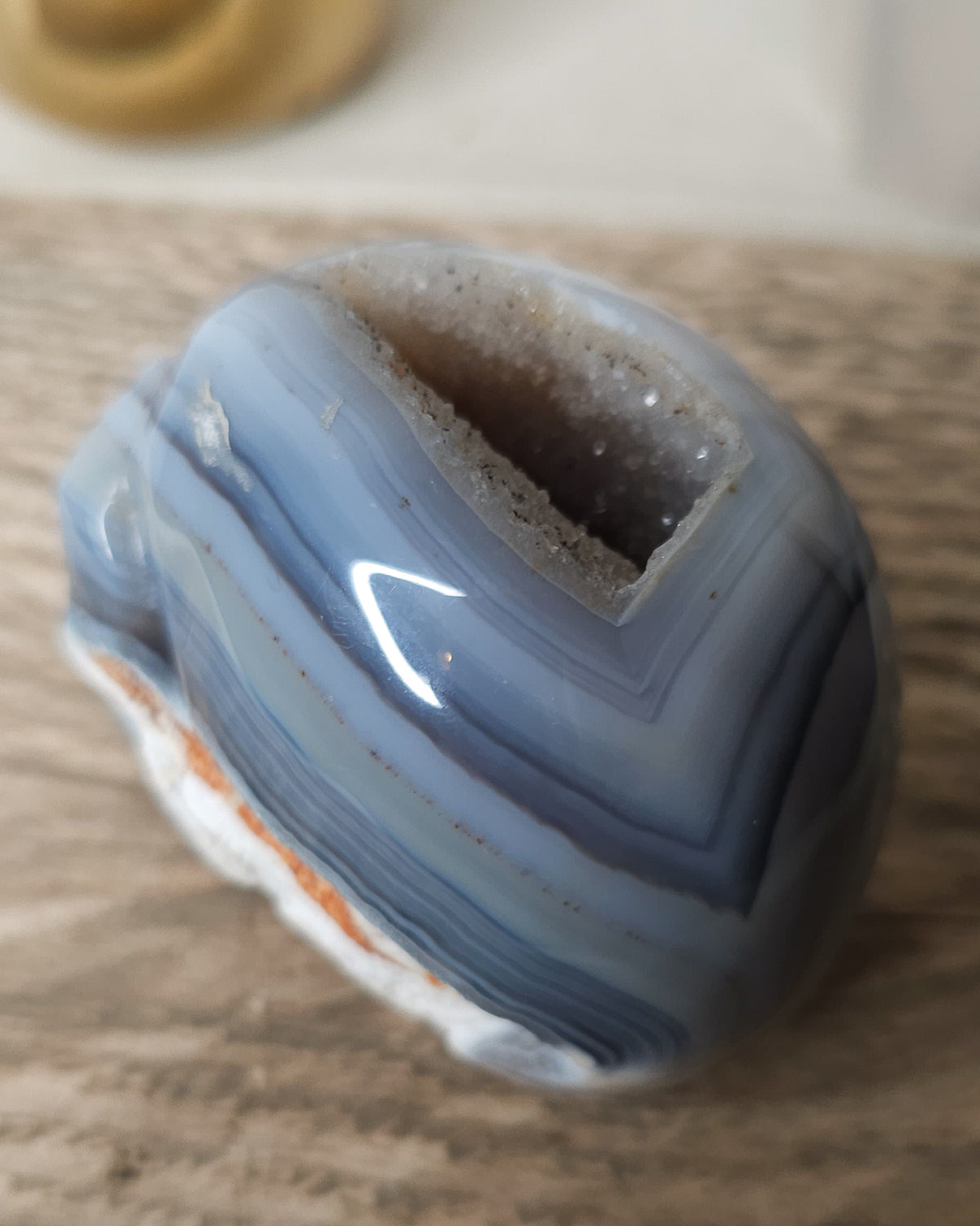 Blue Agate skull carving with layered pale blue and grey bands, a natural brown inclusion along the side and a sparkling druzy crystal cavity at the top.