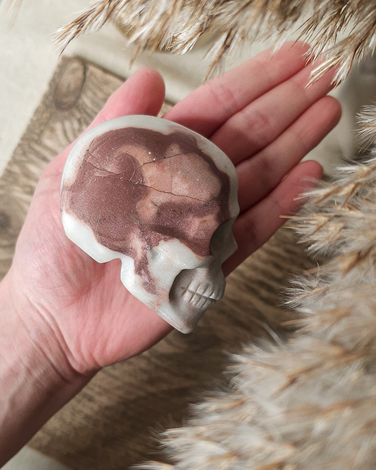 Mookaite crystal skull carving with natural burgundy, dusty pink, cream and grey patterns, polished finish and detailed teeth.