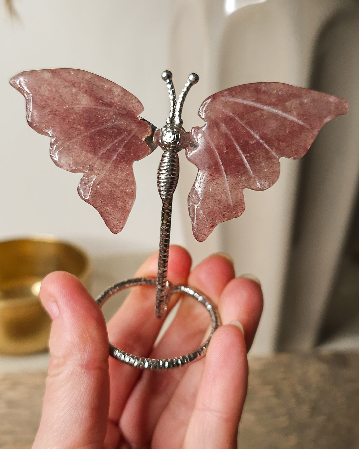 Strawberry Quartz butterfly carving on a silver metal stand, featuring soft rosy pink tones and delicate natural inclusions.