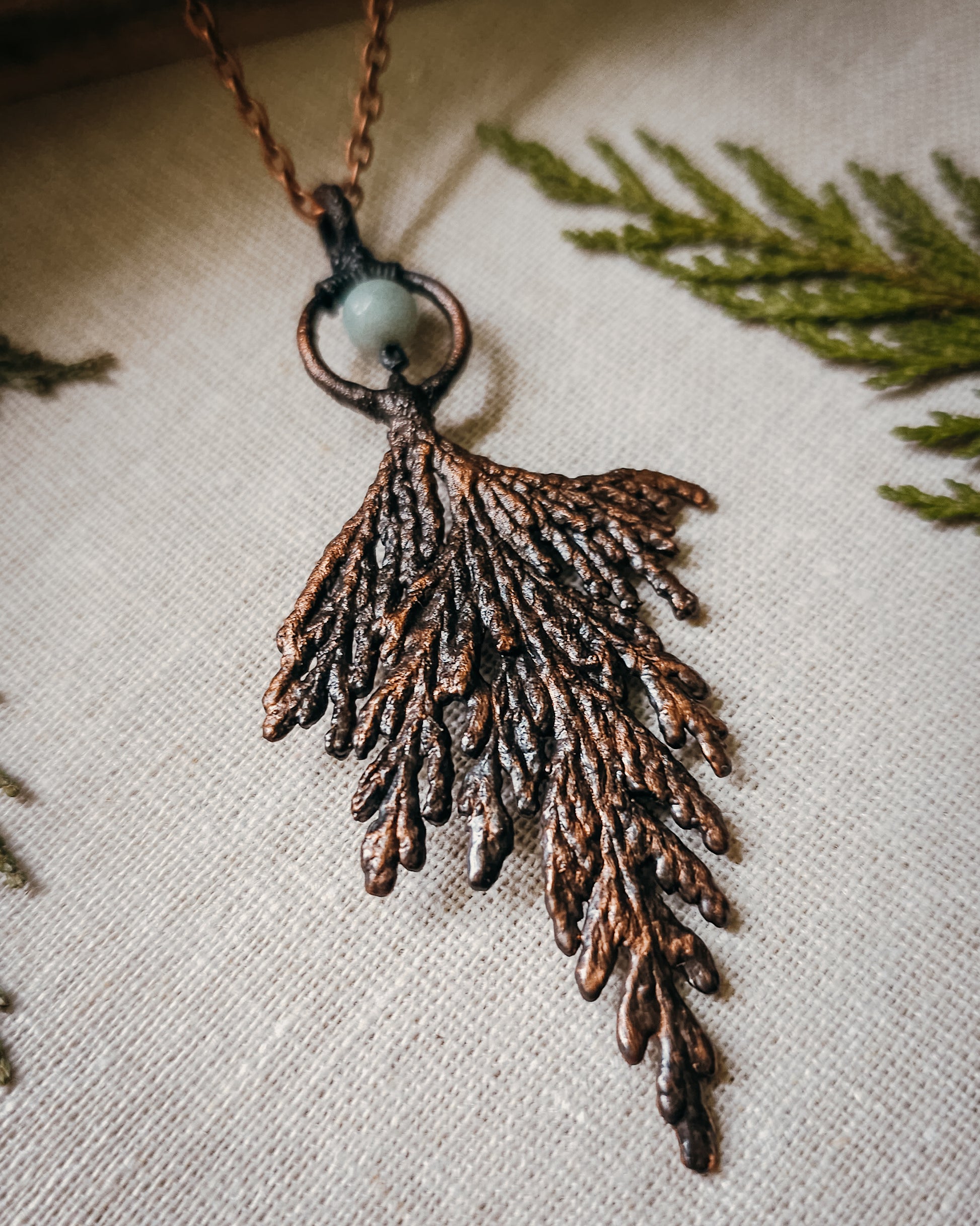 Handmade Copper electroformed Necklace with a cypress and Amazonite bead on a textured fabric background