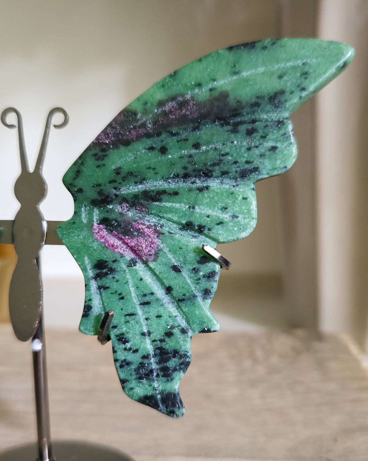 Ruby in Zoisite butterfly wings with fluorescent Ruby inclusions on a black metal stand, glowing vivid pink-red under UV light.