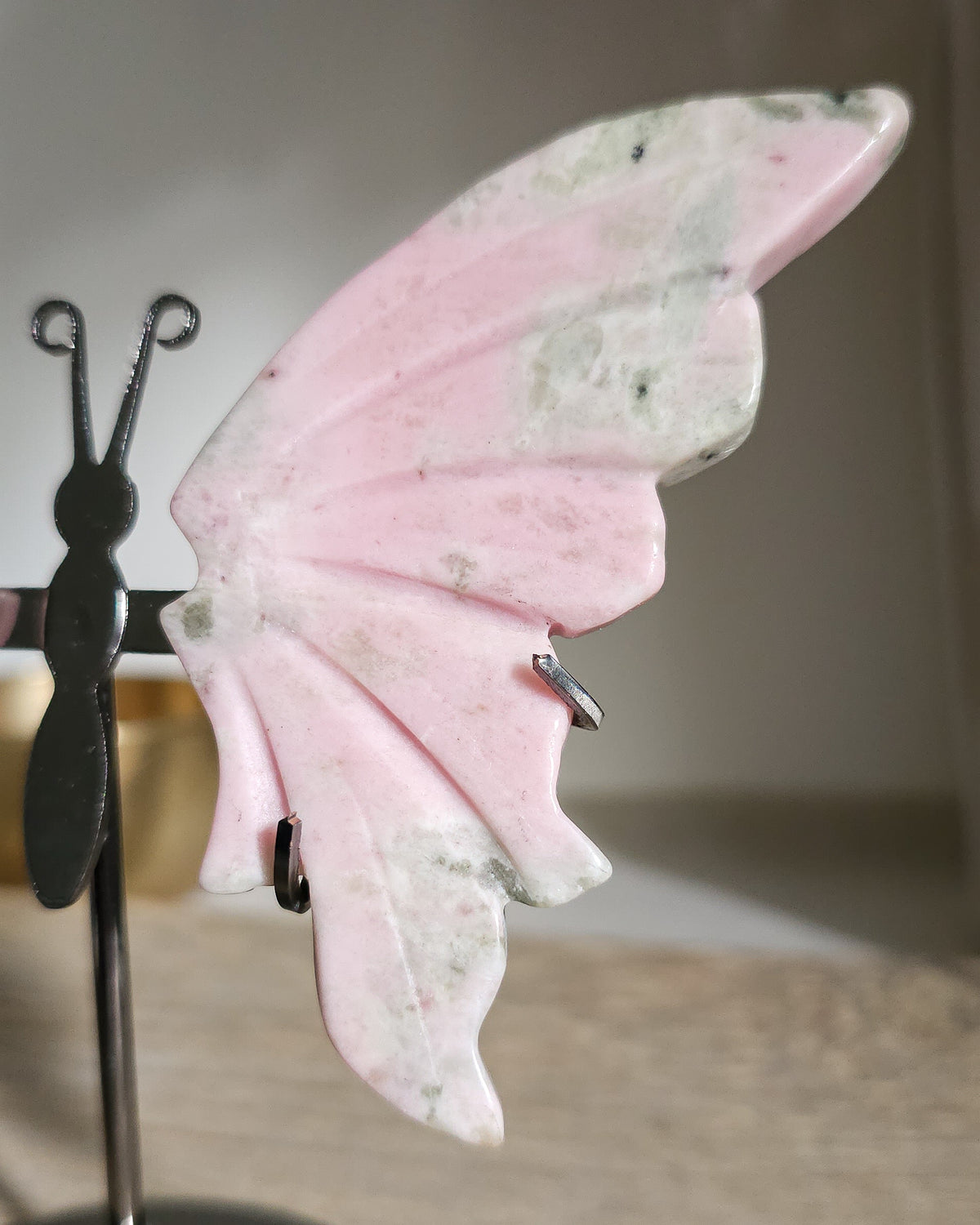 Pink Opal butterfly wings carved from natural pink opal, displayed on a black metal stand, showing soft pink and creamy tones.