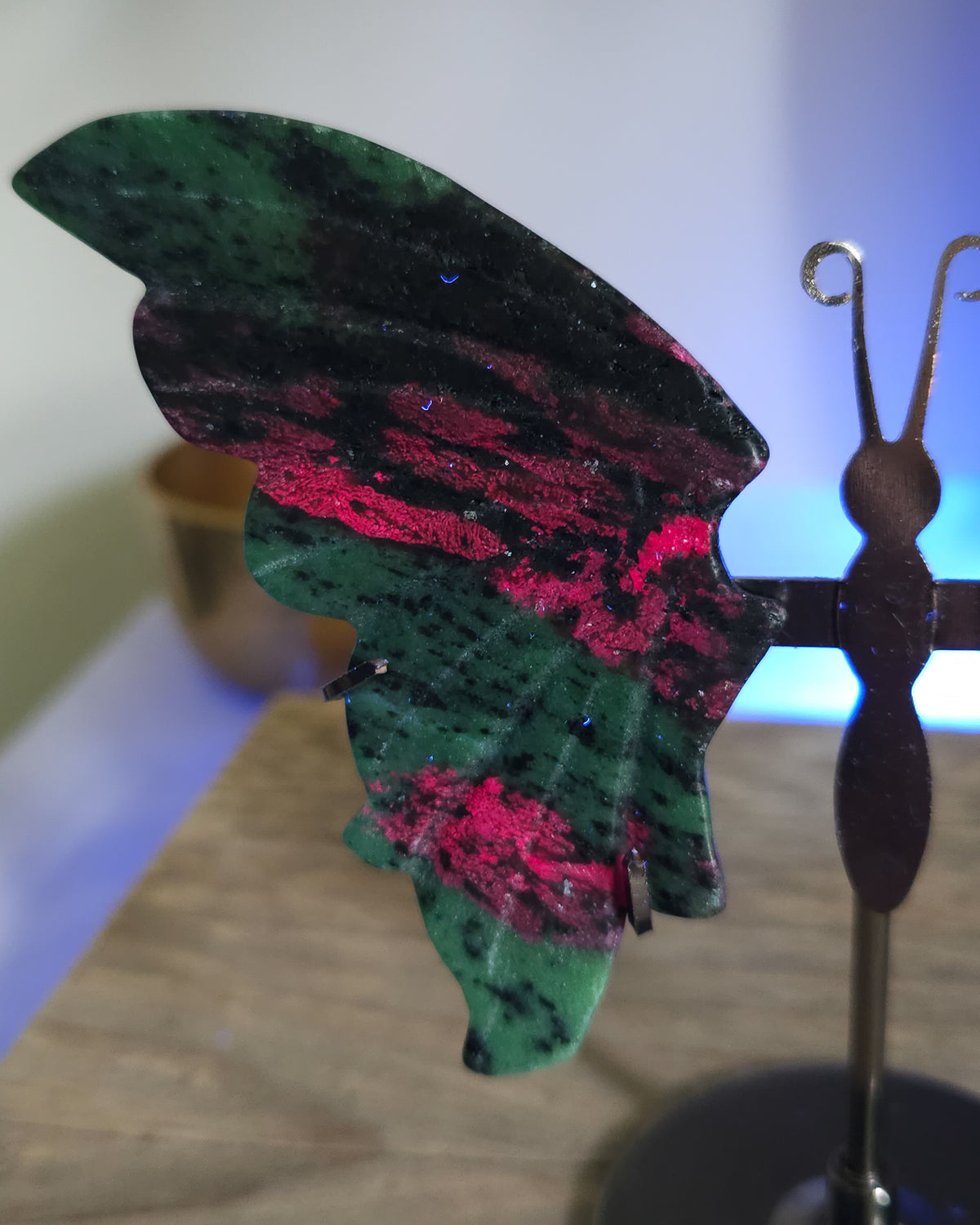 Ruby in Zoisite butterfly wings with fluorescent Ruby inclusions on a black metal stand, glowing vivid pink-red under UV light.