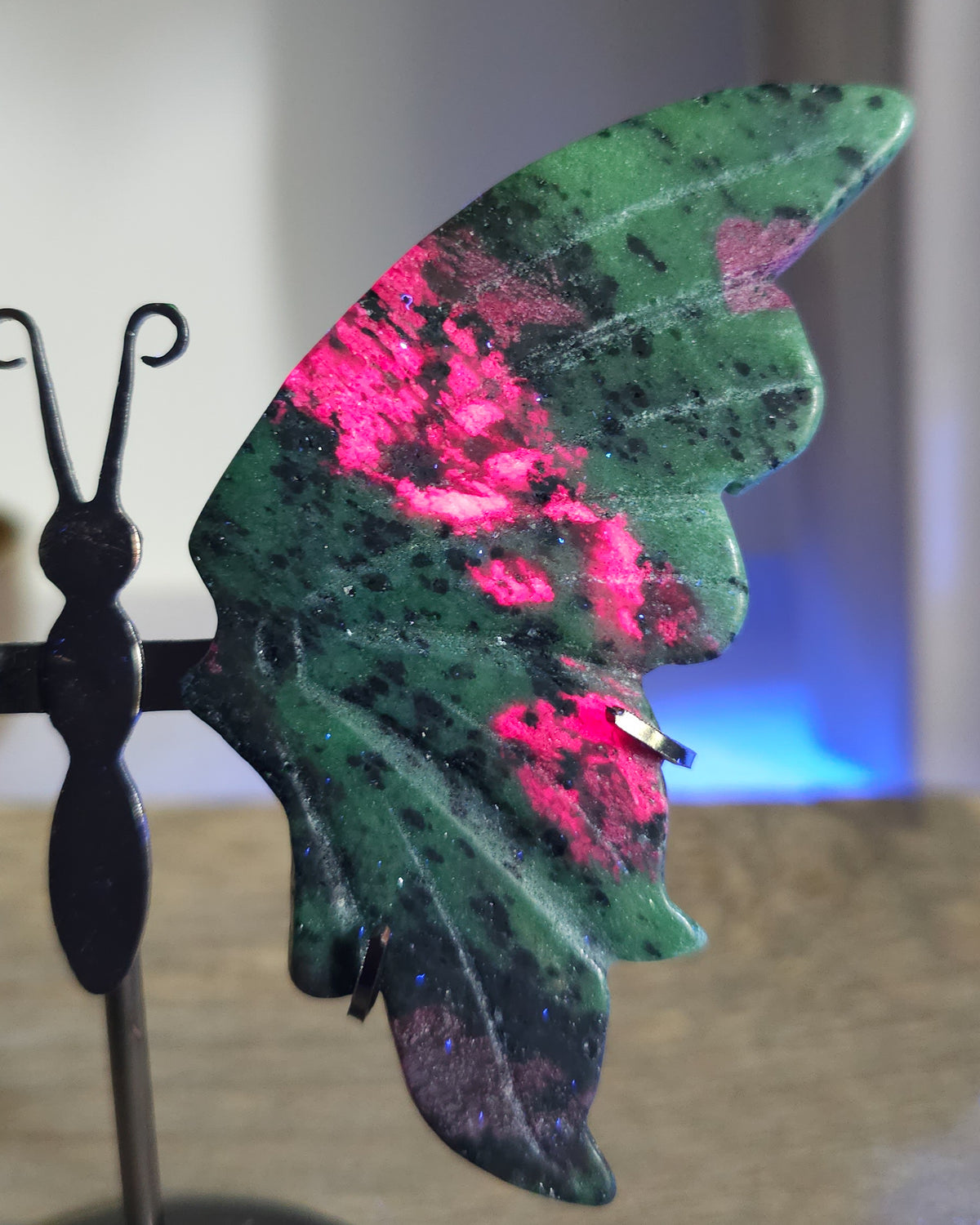 Ruby in Zoisite butterfly wings with fluorescent Ruby inclusions on a black metal stand, glowing vivid pink-red under UV light.