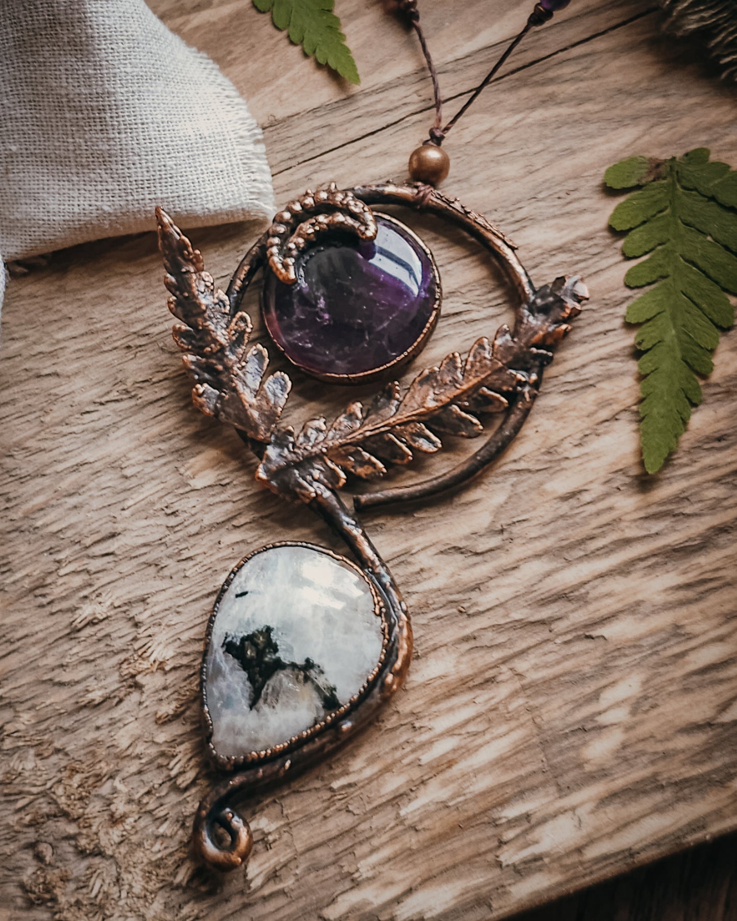 Copper electroformed Ornate pendant with amehtyst, Moonstone and fern leaves on a wooden surface with leaves