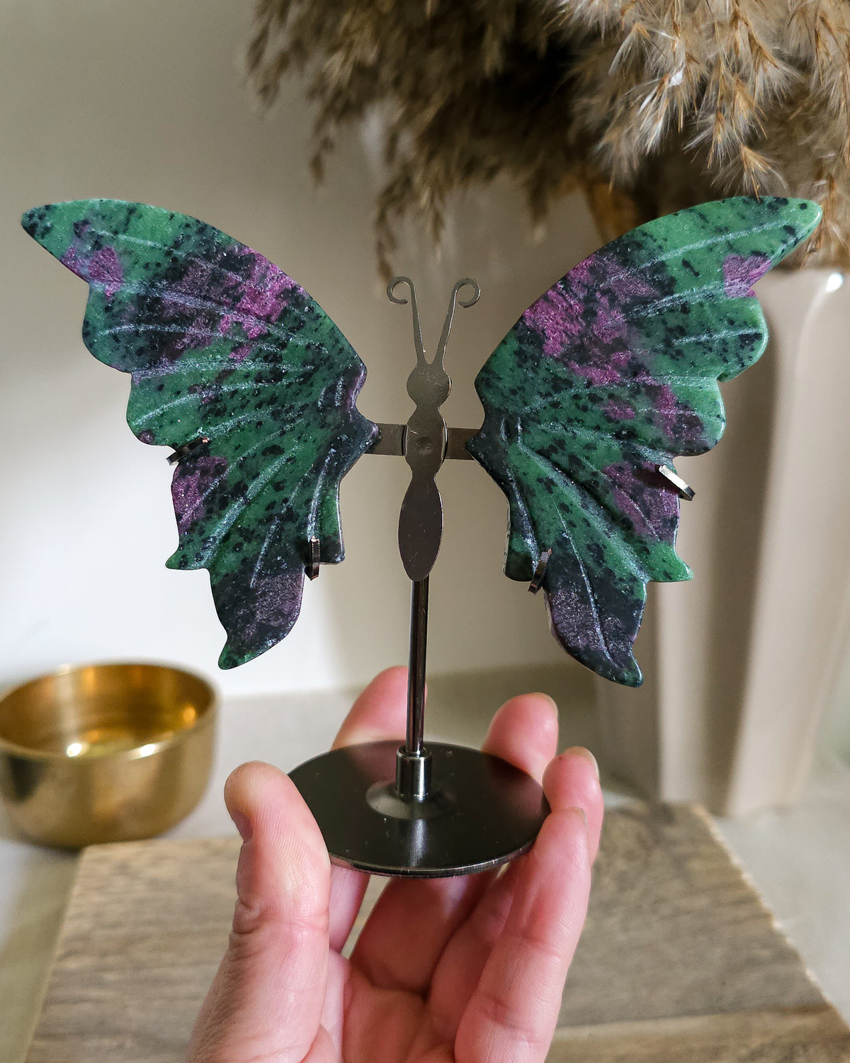 Ruby in Zoisite butterfly wings with fluorescent Ruby inclusions on a black metal stand, glowing vivid pink-red under UV light.