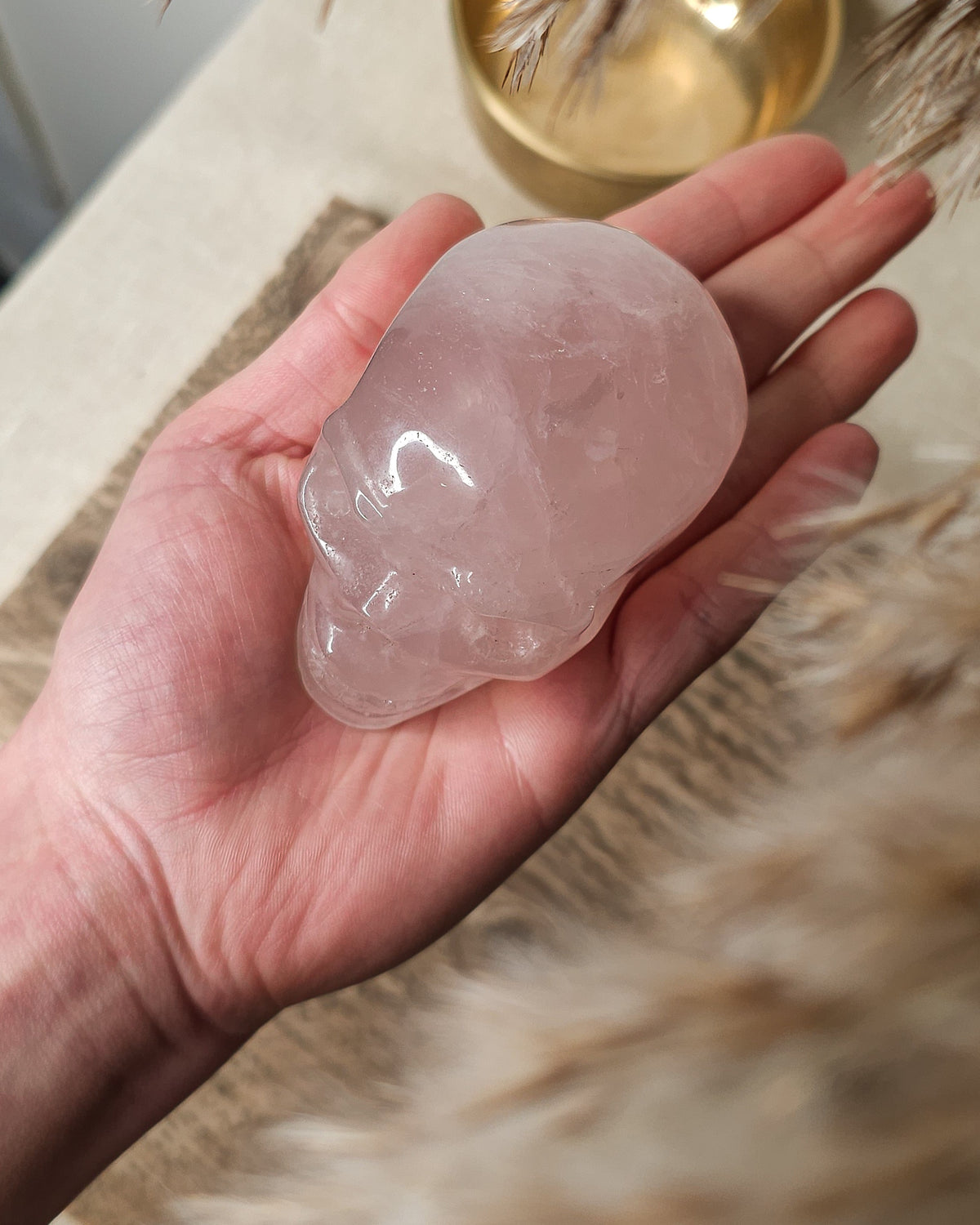 Rose Quartz crystal skull carving with soft pink tones and natural cloudy patterns, polished finish, displayed as a decorative crystal piece.